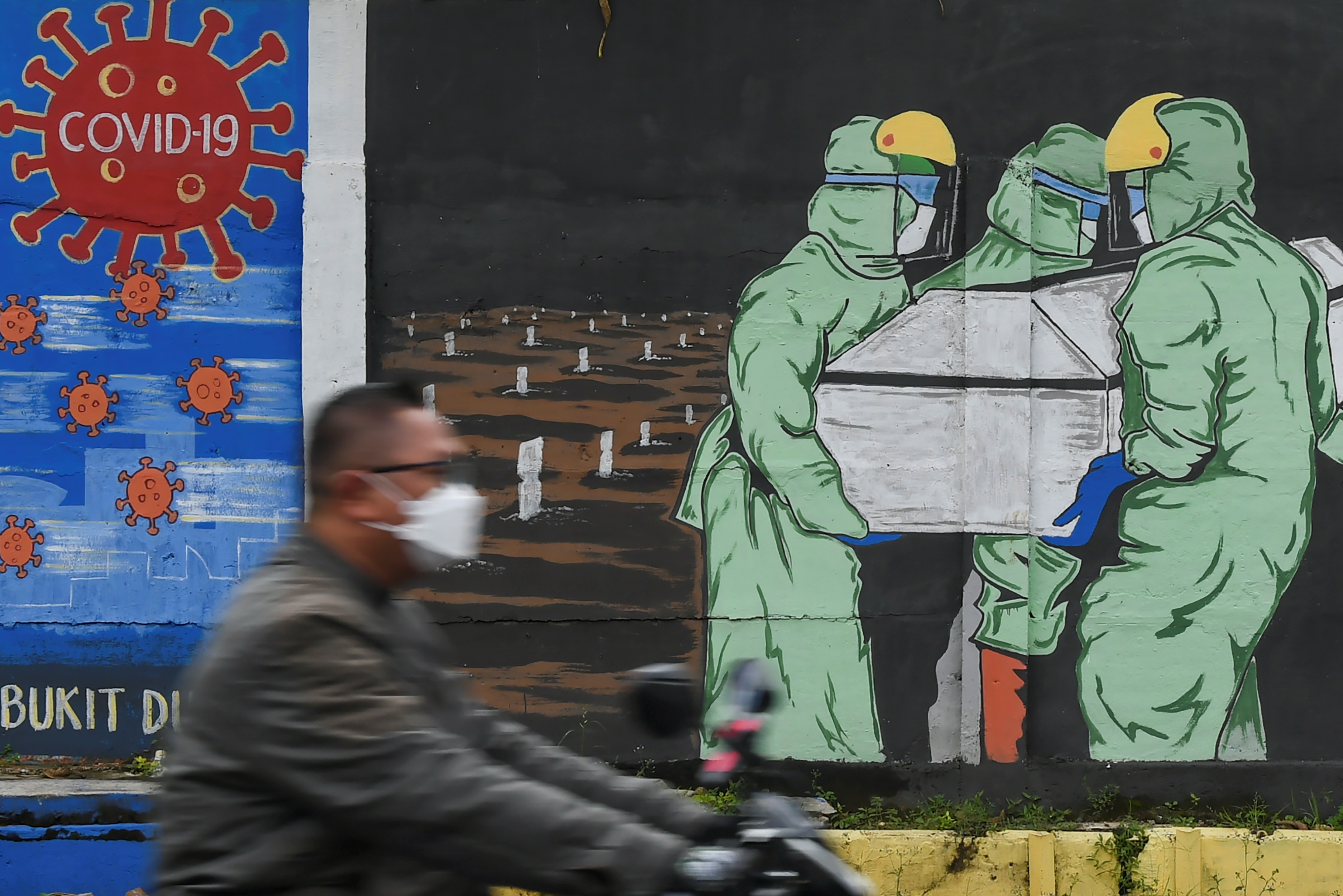 Pengendara sepeda motor melintas di depan mural tentang pandemi covid-19 di Bukit Duri, Jakarta.