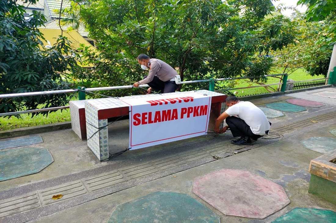 Dua anggota Polresta Jambi mamasang banner bertuliskan ditutup selama PPKM di salah satu bangku permanen di Kota Jambi