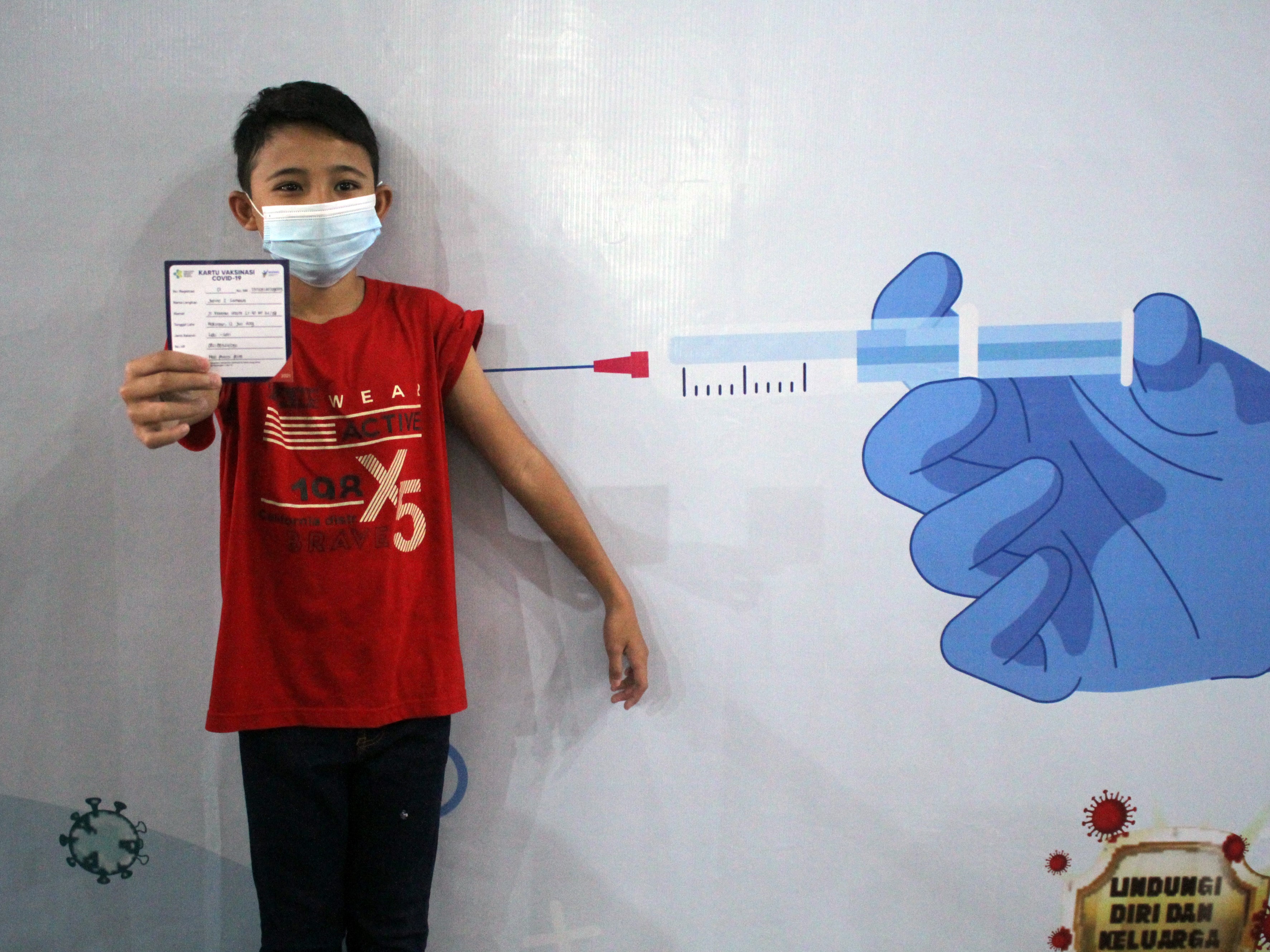 Seorang anak menunjukkan kartu vaksinasi covid-19.