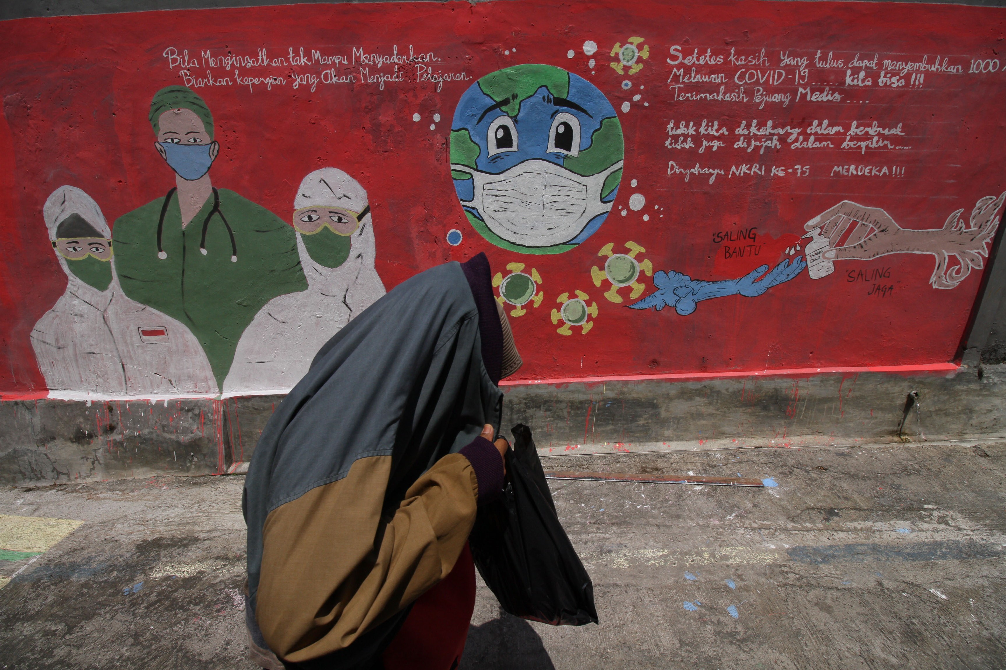 Seorang warga melintas di depan mural kampanye untuk melawan covid-19 di kawasan Depok, Jawa Barat.