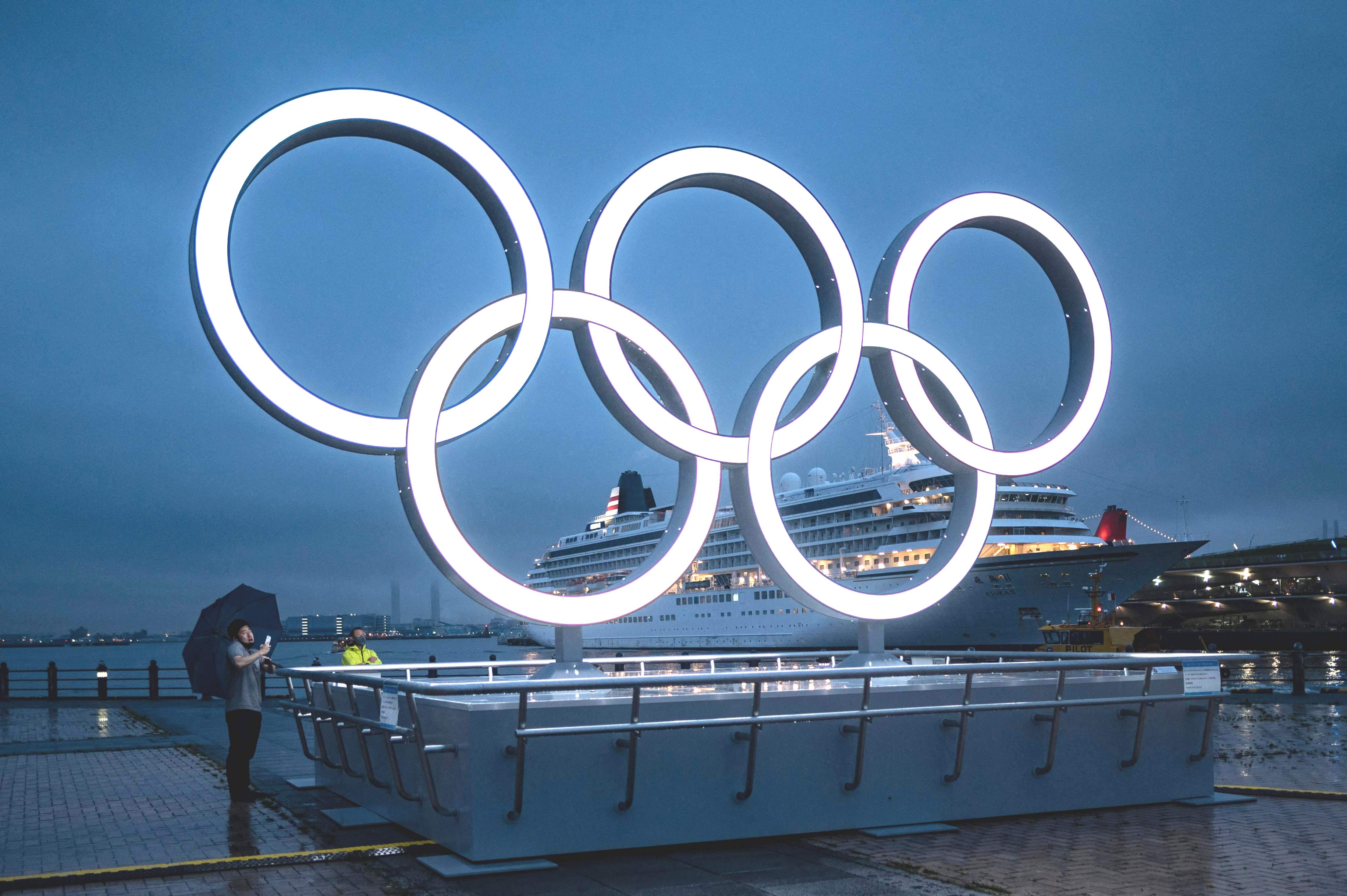 Seorang pria berdiri dekat dengan lingkaran simbol Olimpiade Tokyo di Kota Yokohama, Jepang, Jumat (2/7). 