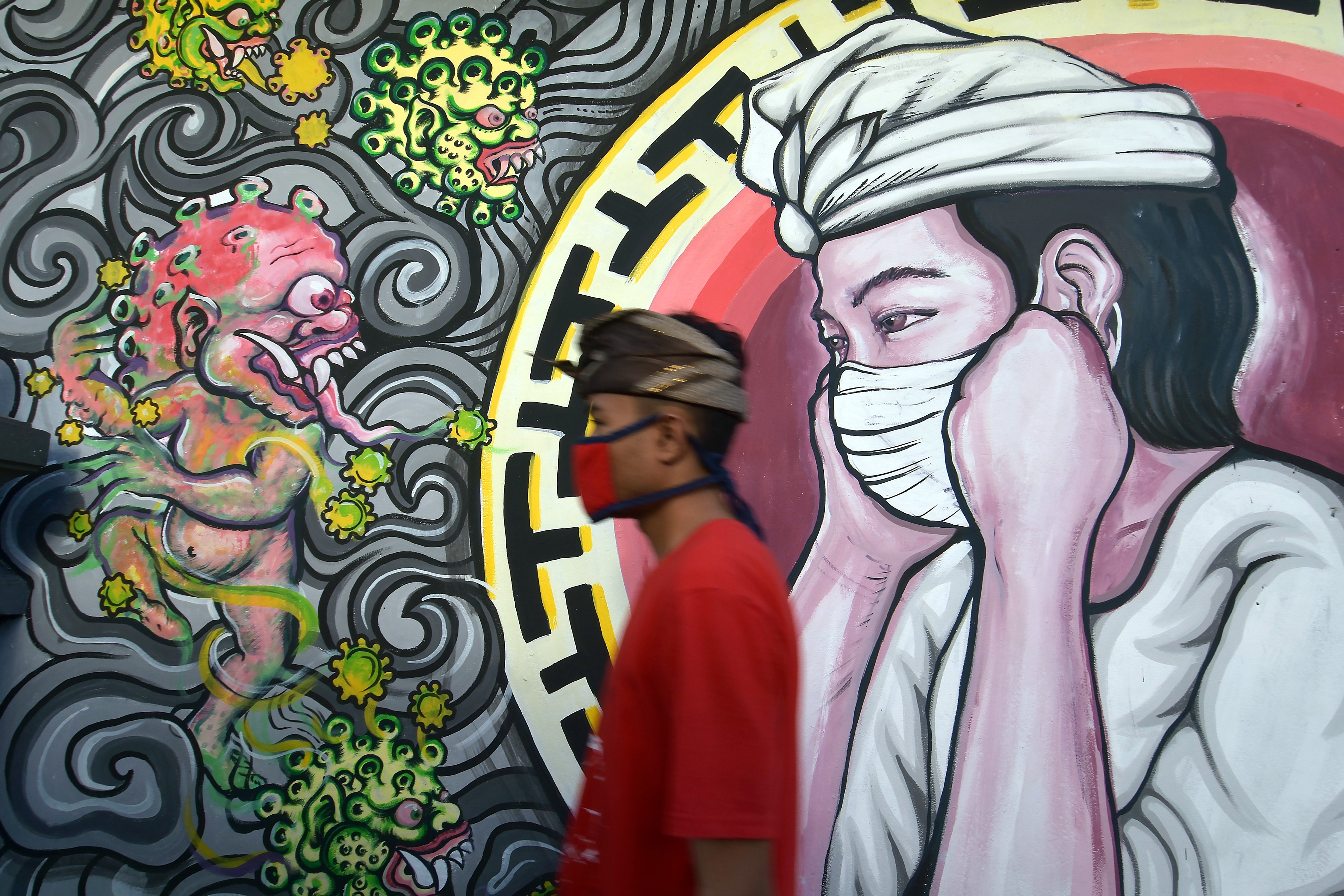 Warga melintas di dekat mural bergambar monster covid-19 berhadapan dengan umat Hindu yang menggunakan masker di Denpasar, Bali.