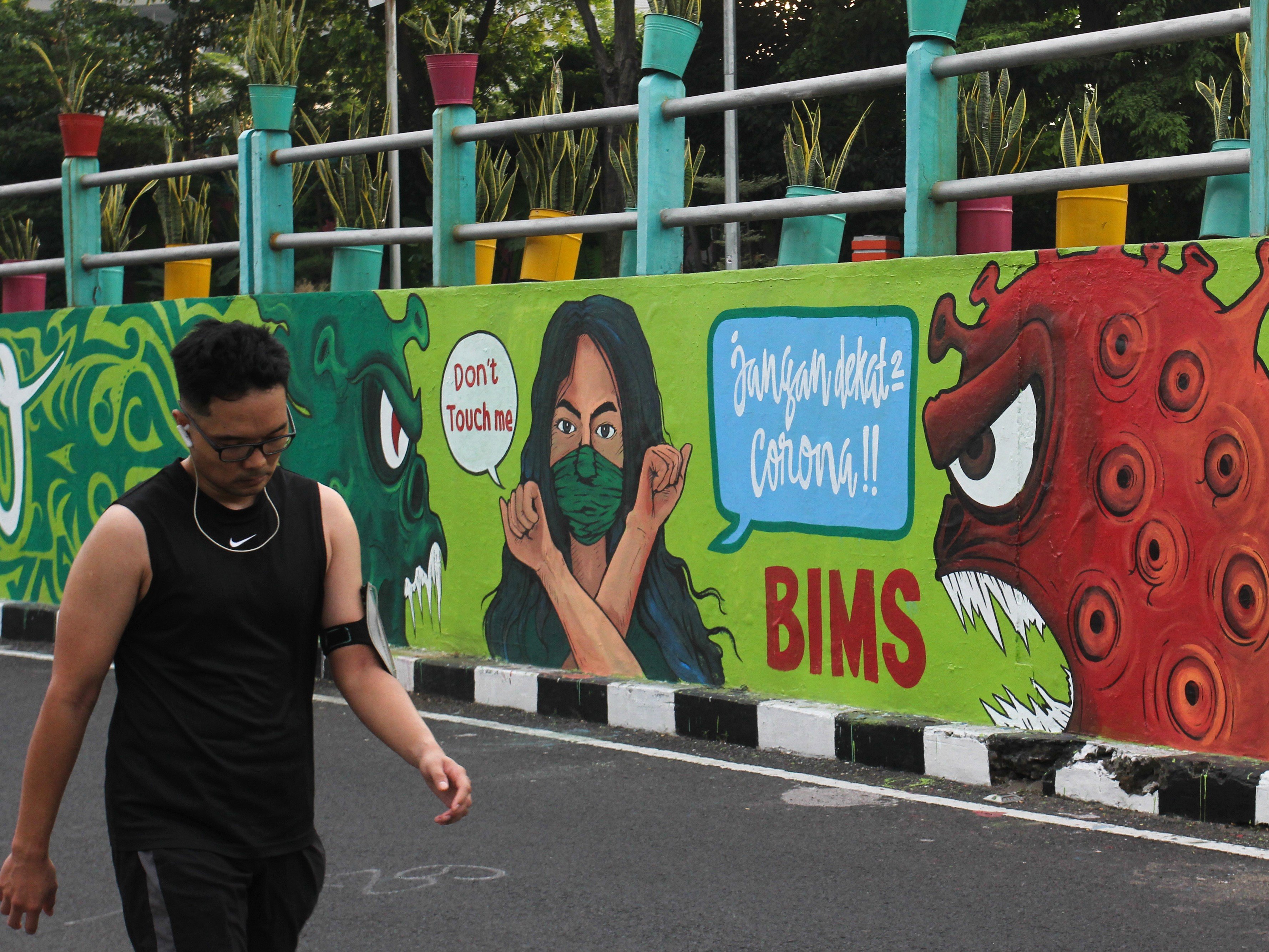 Warga berjalan di dekat dinding bermural di Surabaya, Jawa Timur, Minggu (18/7).