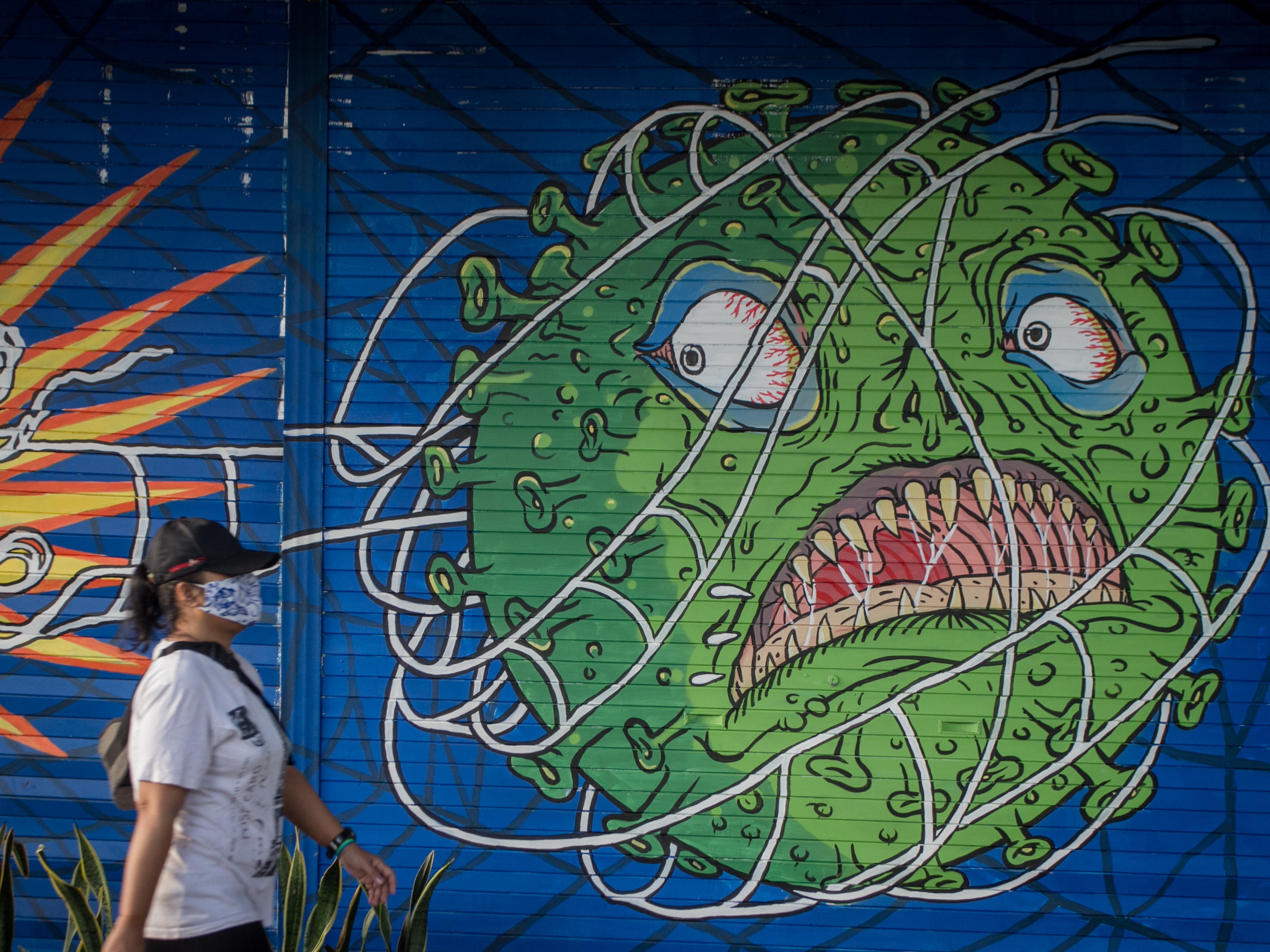 Warga melintas di depan mural bertema covid-19 di Kemplayan, Solo, Jawa Tengah.