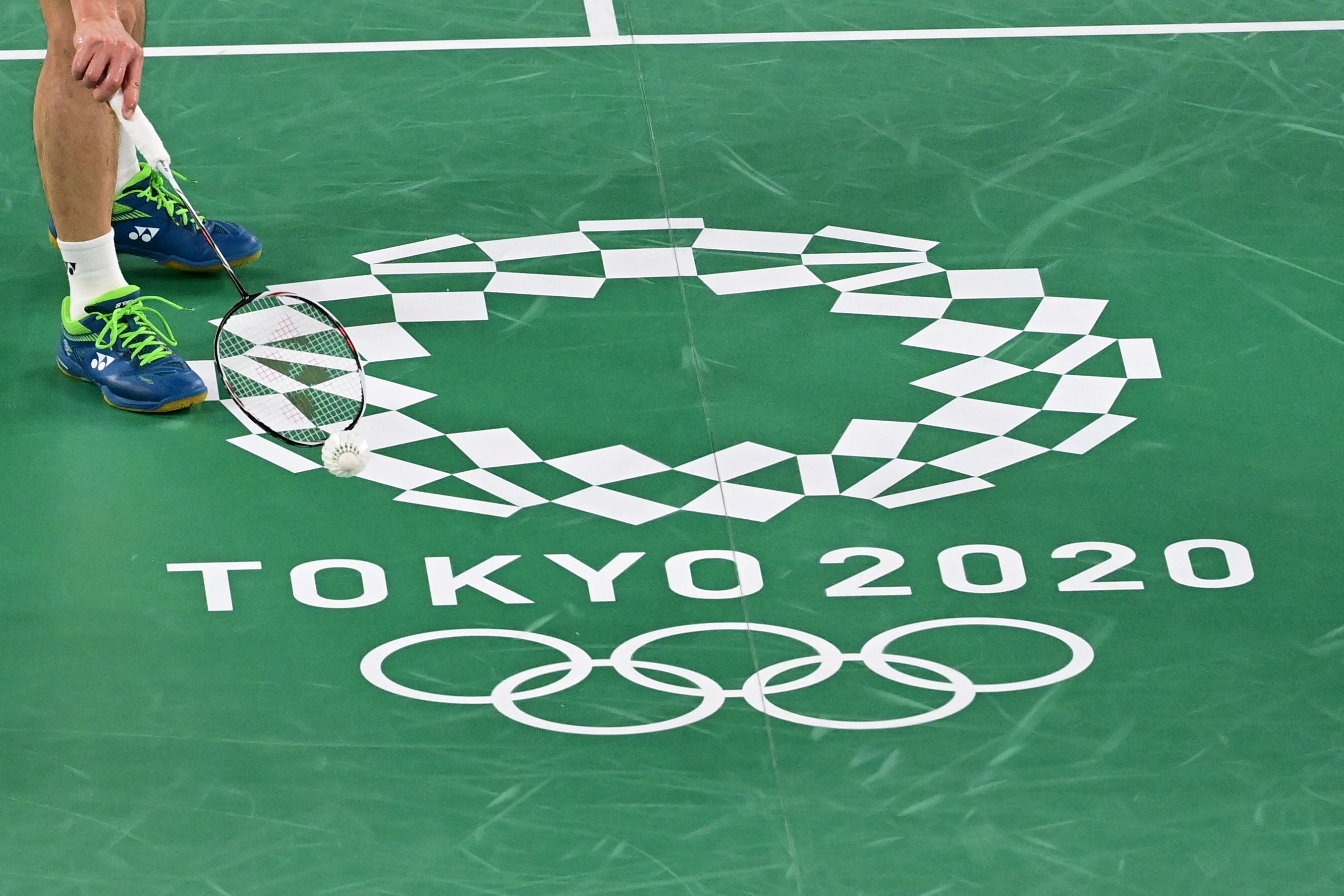 Seorang atlet bulu tangkis berdiri di dekat logo Olimpiade Tokyo 2020.
