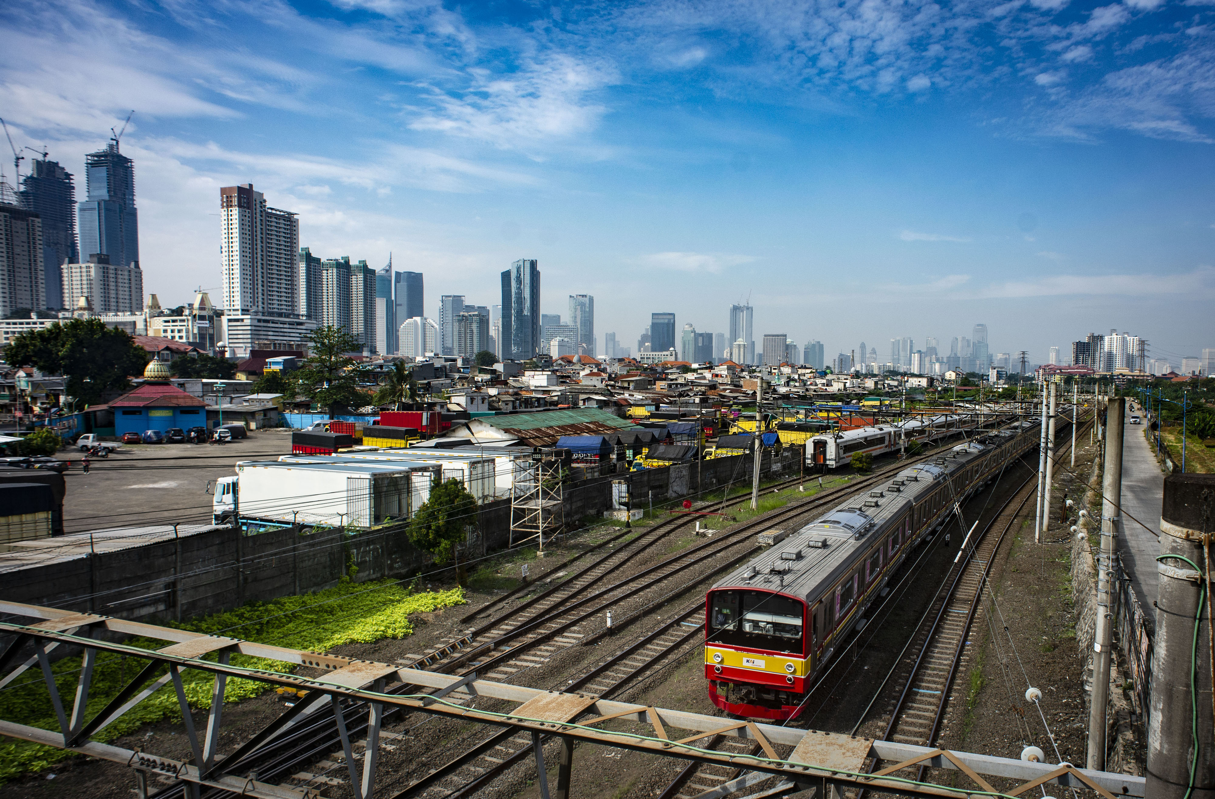 KRL melintas dengan latar belakang permukiman penduduk dan gedung bertingkat di wilayah Jakarta.