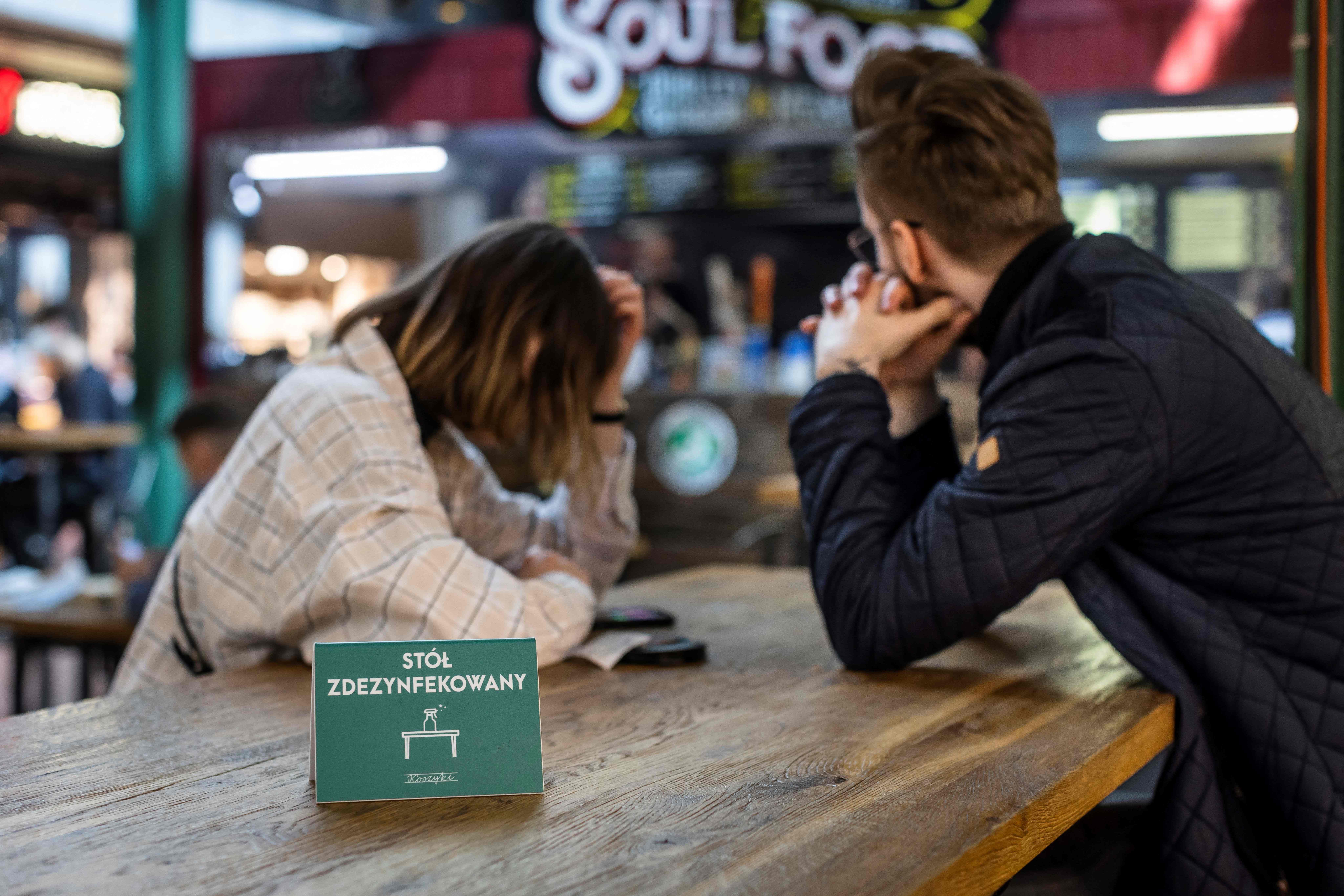 Dua warga menunggu di meja bertuliskan 'Sudah didisinfeksi' di sebuah restoran di Warsawa, Polandia.