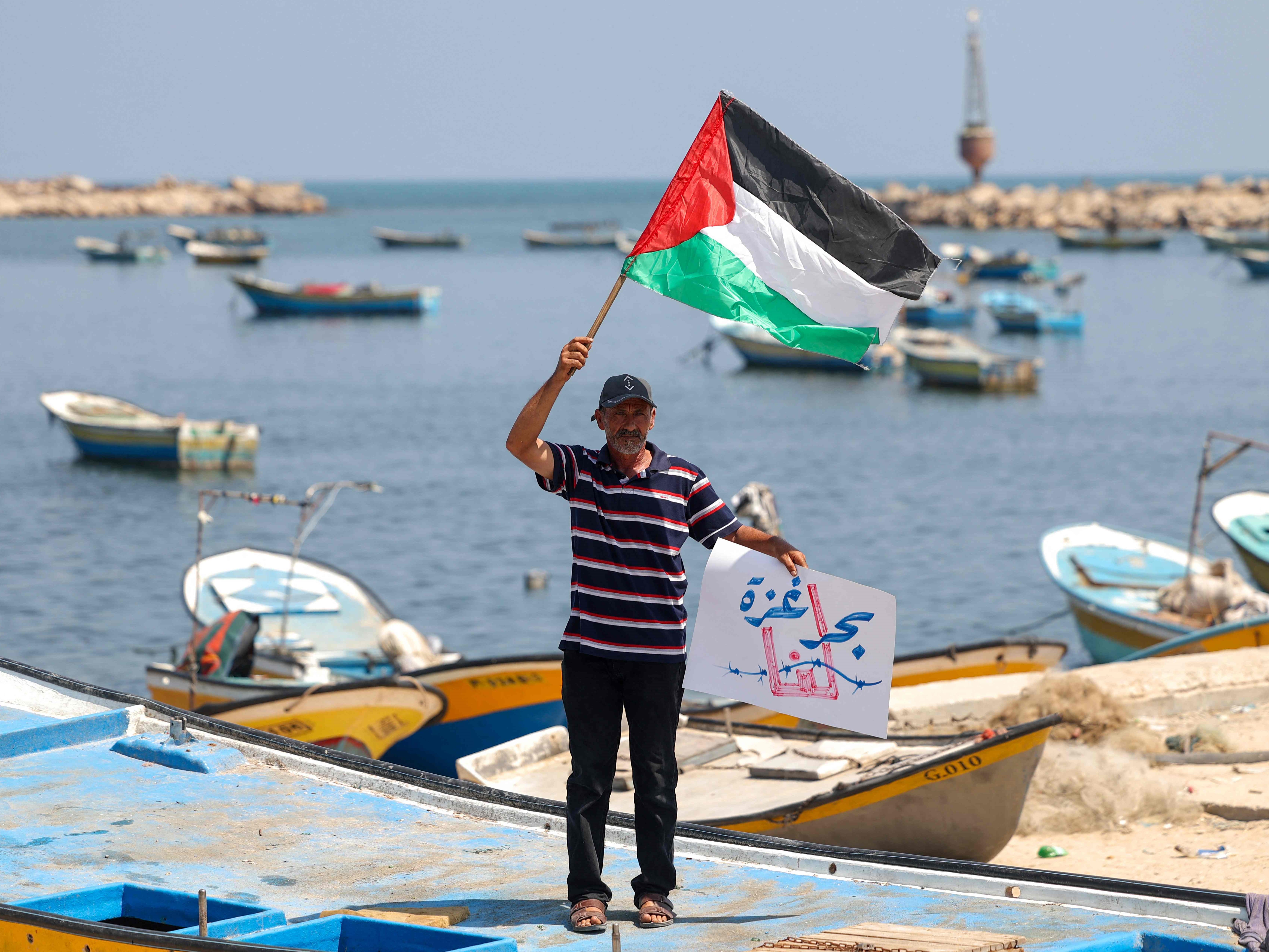 Seorang nelayan Palestina mengibarkan bendera Palestina selama protes terhadap blokade di Gaza di pelabuhan Kota Gaza pada 11 Juli 2021.