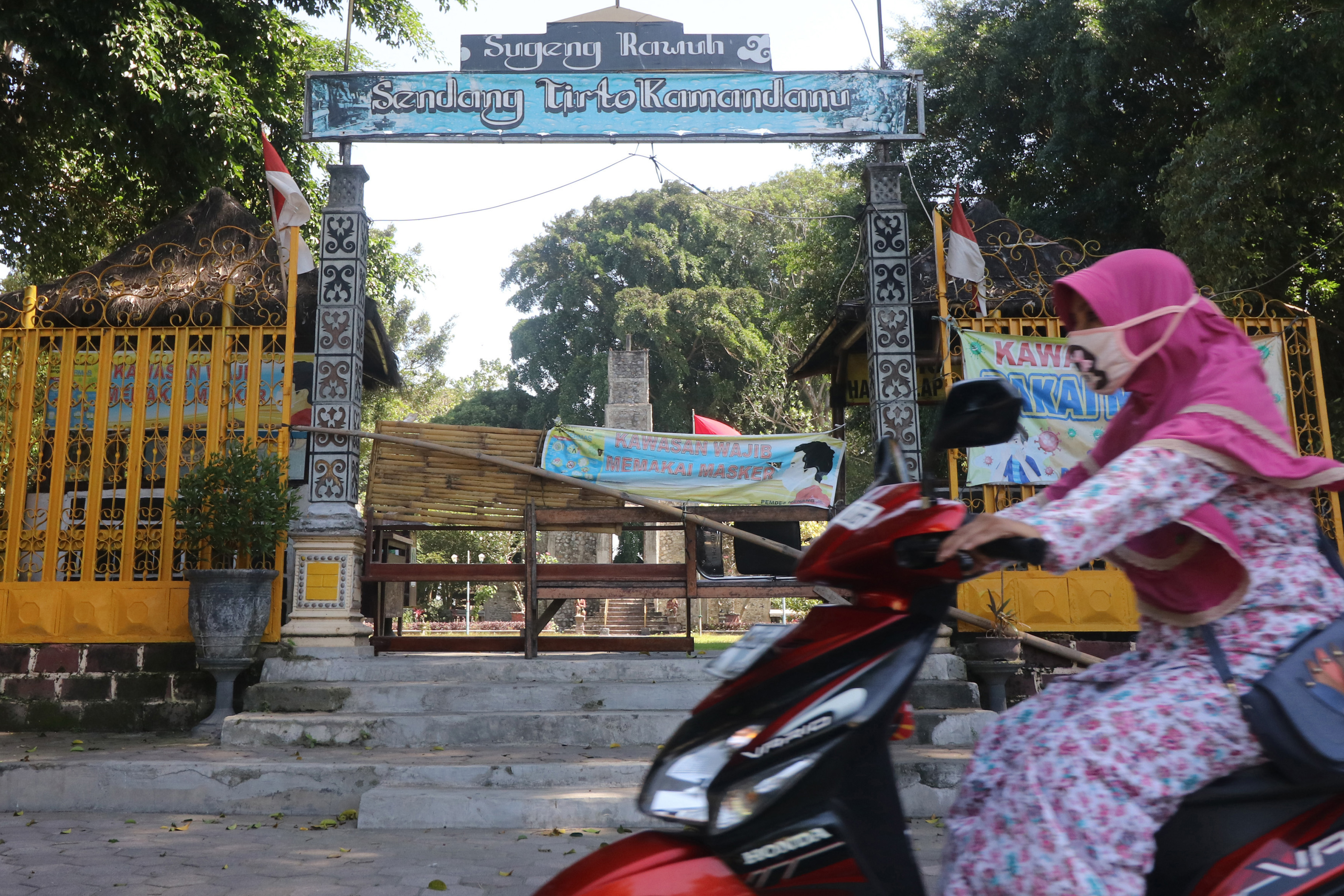 Warga melintas di depan pintu gerbang wisata Sendang Tirto Kamandanu, Desa Menang, Kediri.