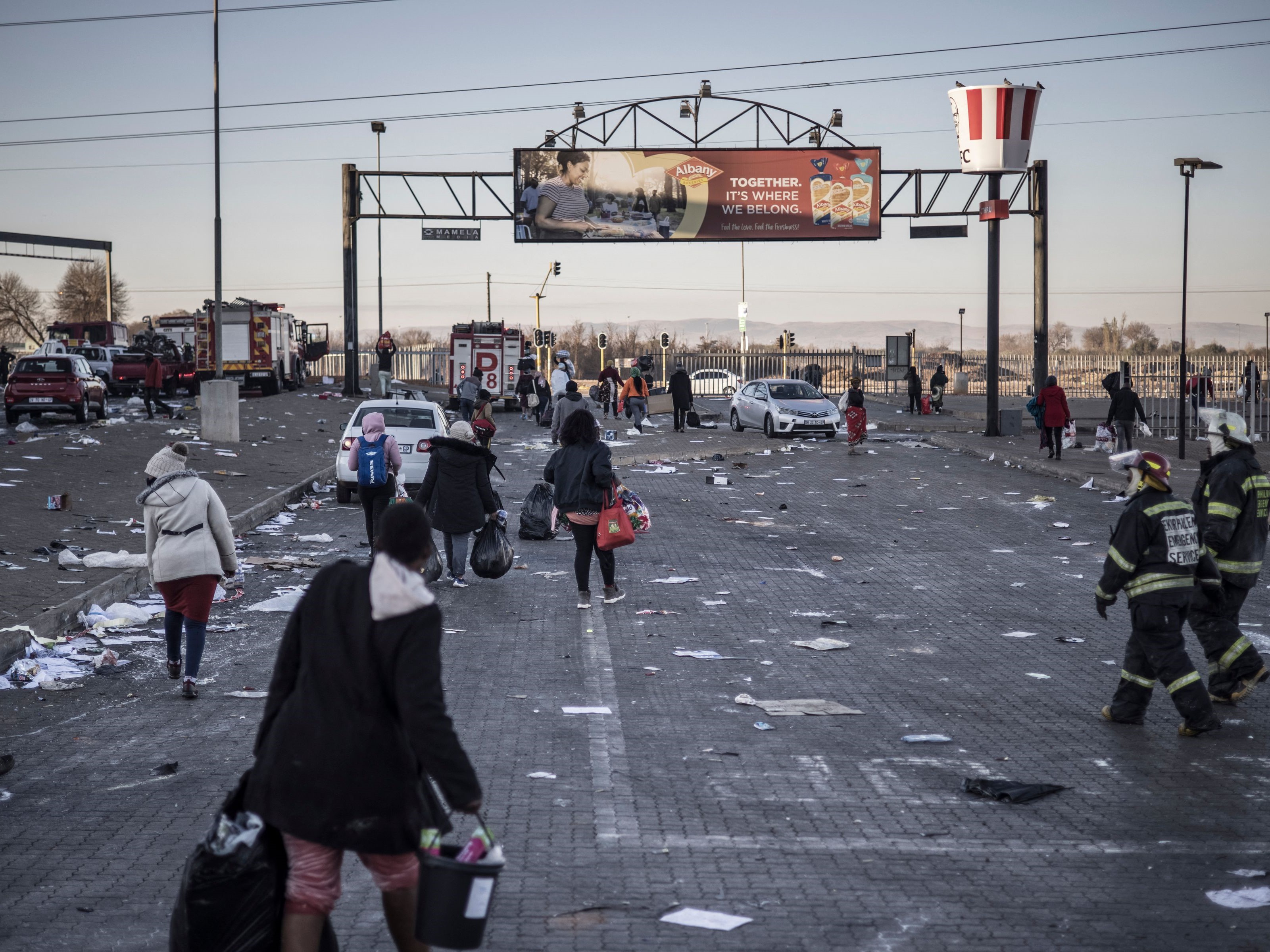 Petugas pemadam kebakaran Afrika Selatan (kanan) mengawasi penjarah berjalan di luar mal yang dirusak di Vosloorus.