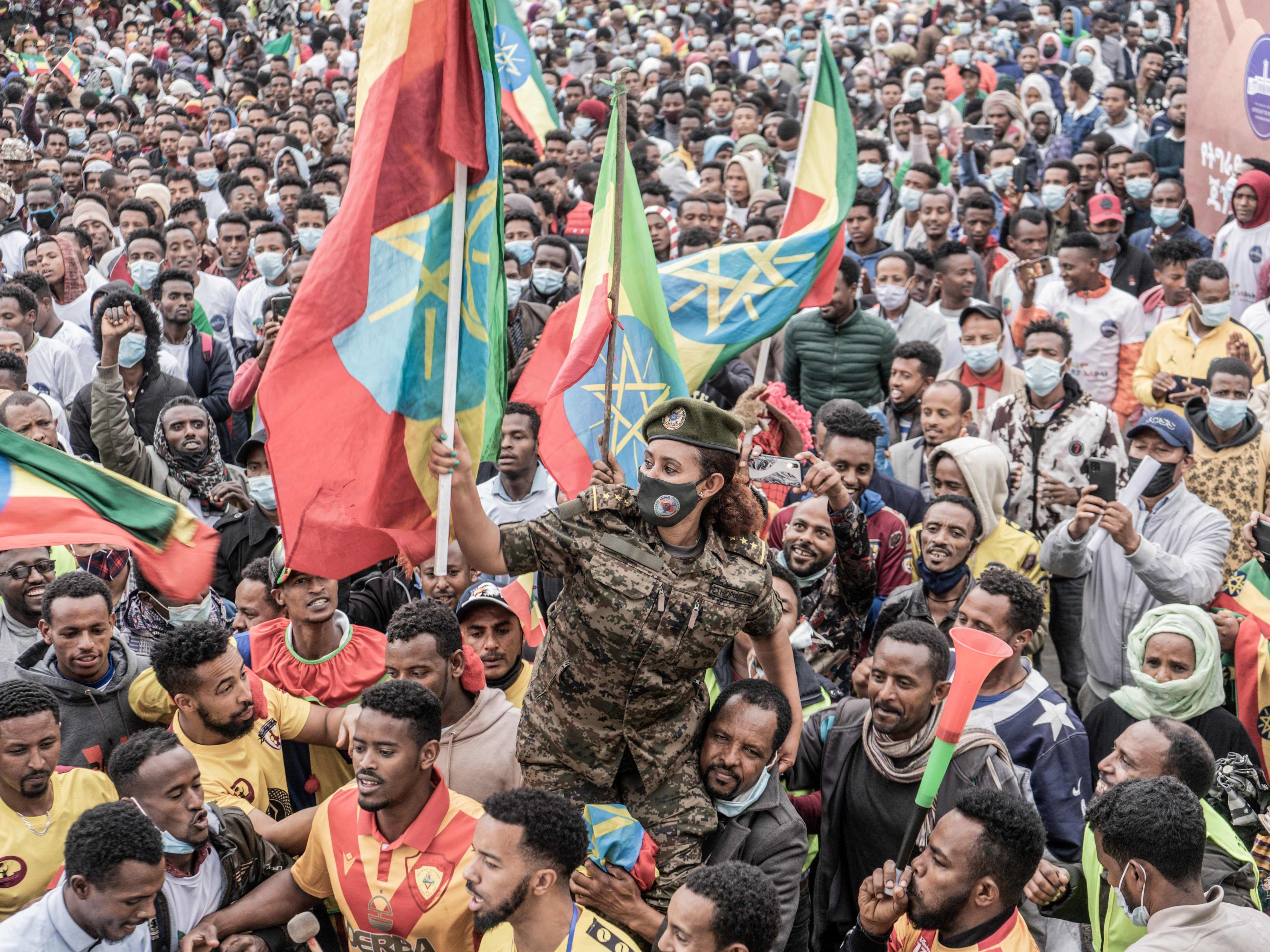 Seorang anggota pasukan militer Ethiopia memegang bendera nasional Ethiopia sambil duduk di bahu anggota militer yang baru direkrut.