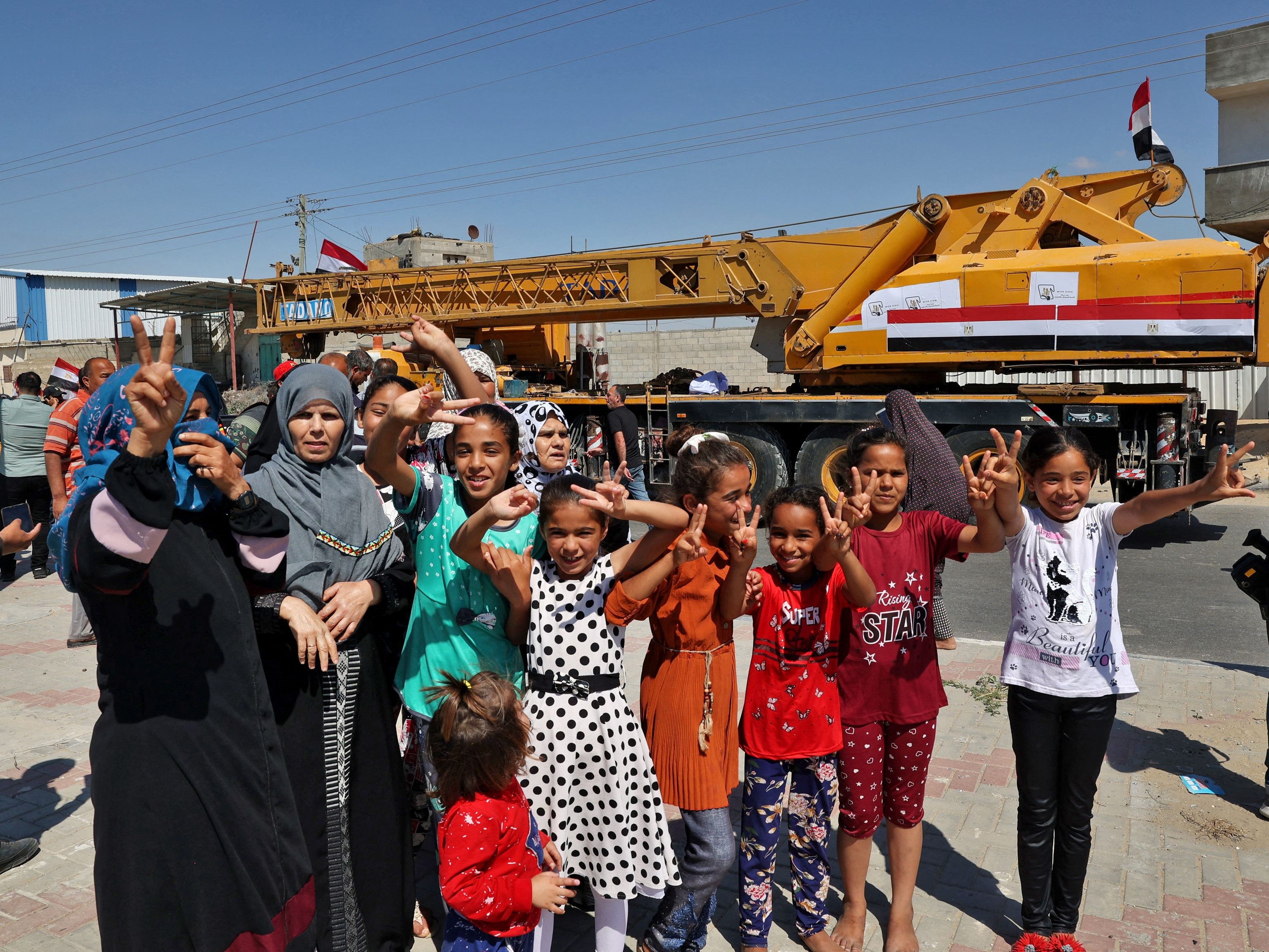 Wanita dan anak-anak Palestina berpose di dekat derek konstruksi (disediakan oleh Mesir) tiba di perbatasan Rafah. 