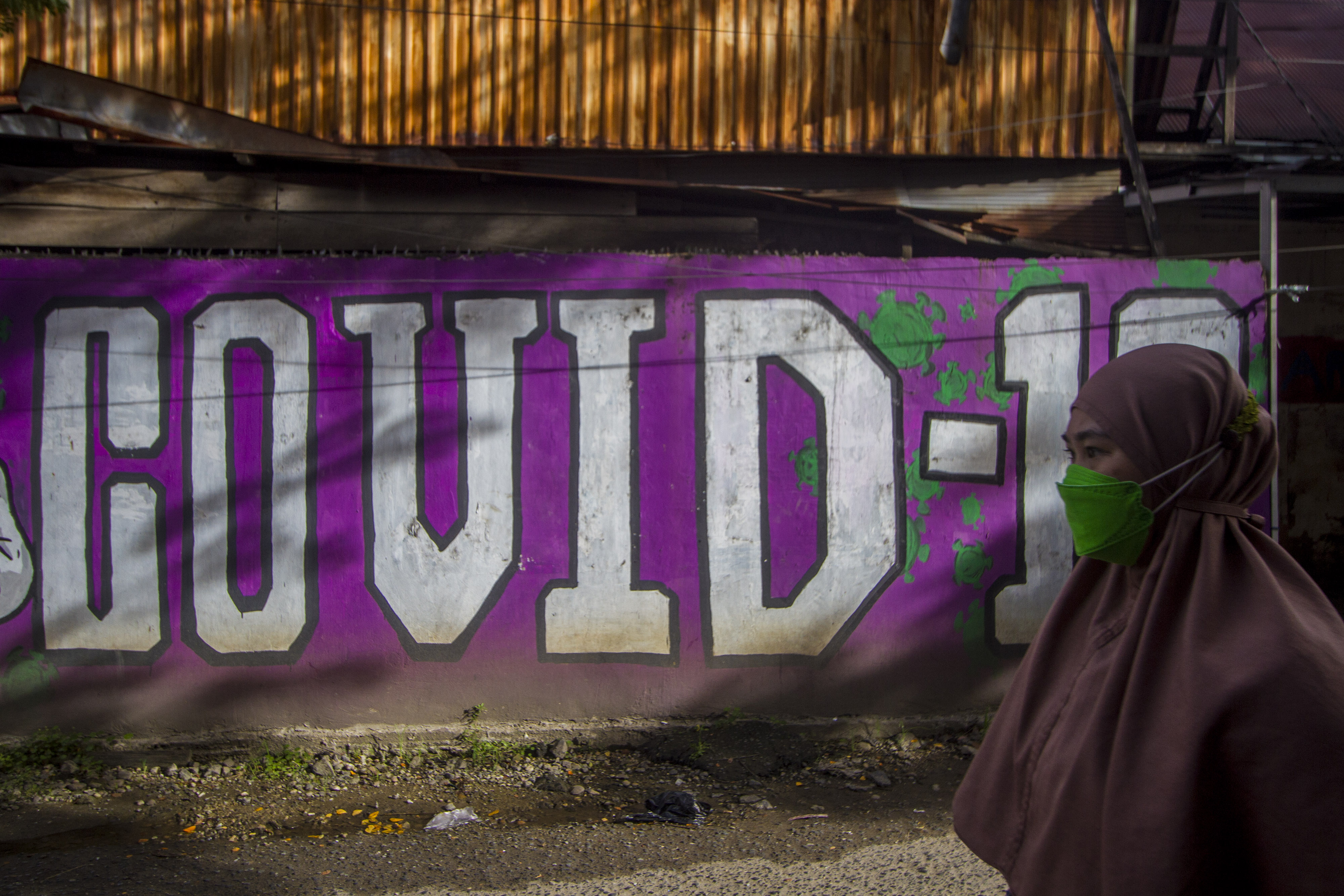 Warga melintas di dekat mural terkait pandemi covid-19 di wilayah Banjarmasin, Kalimantan Selatan.