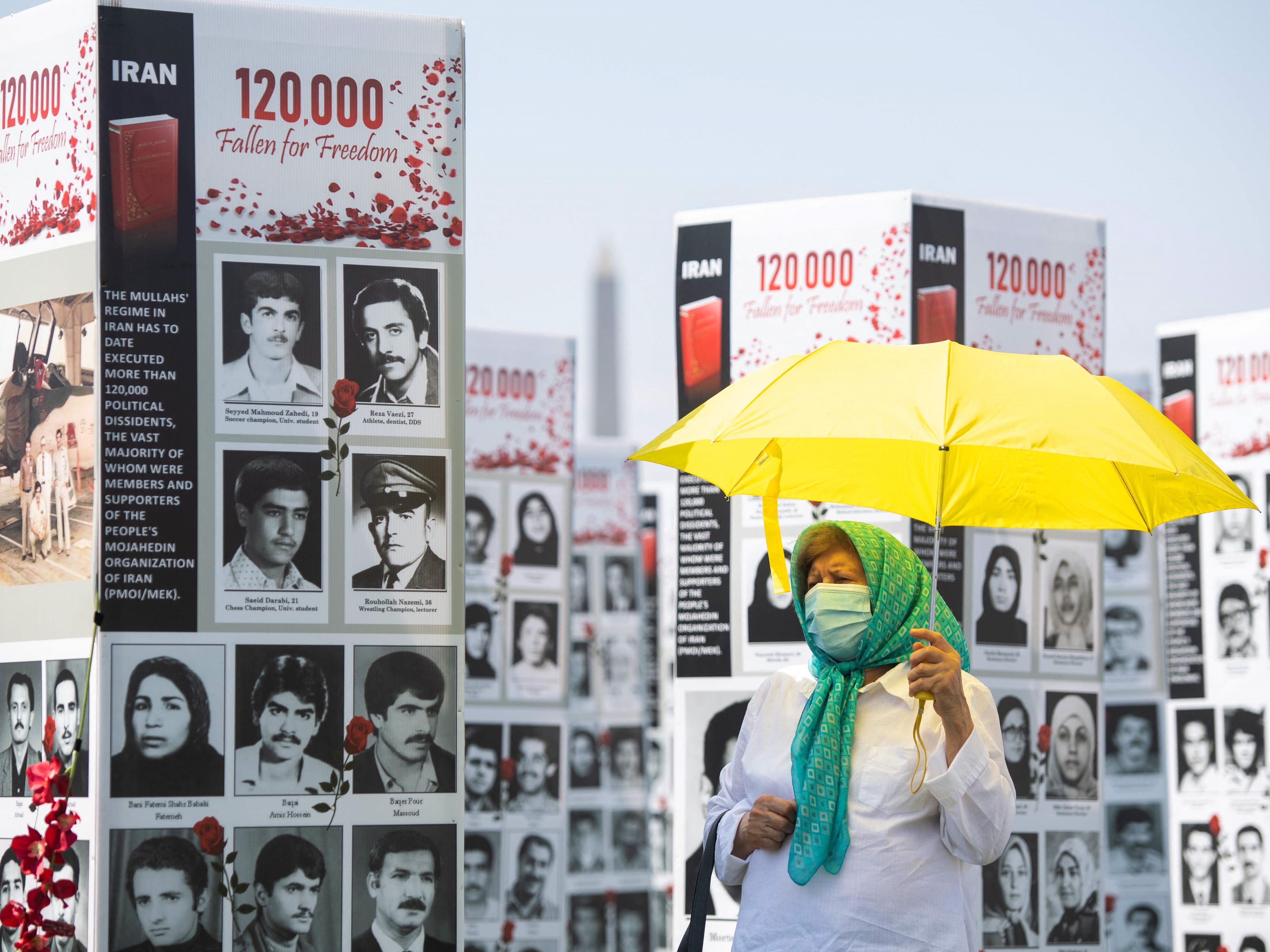 Seorang wanita dengan payung berjalan melewati beberapa dari ribuan foto orang yang terbunuh di Iran pada 1988, di Washington DC, AS.
