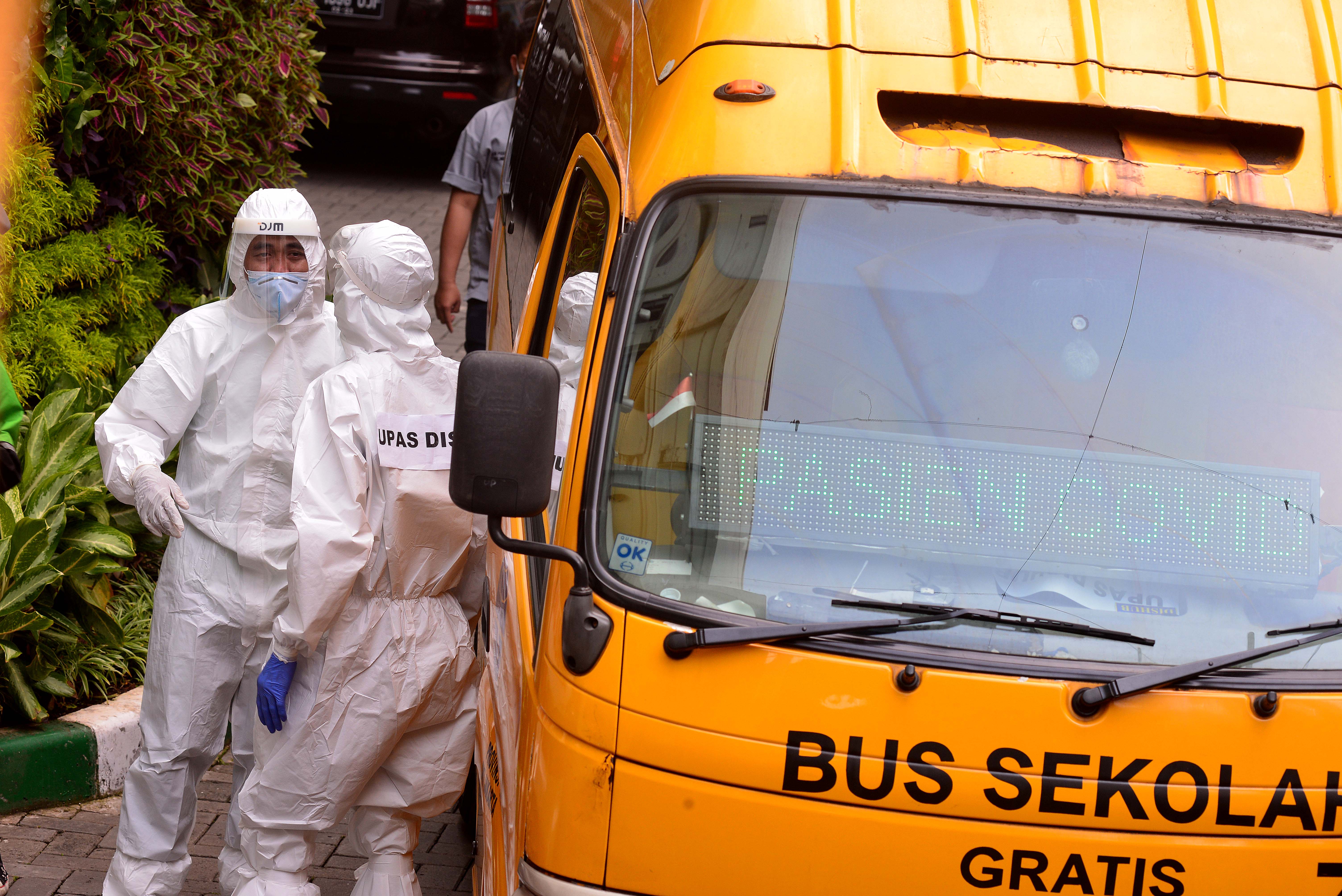 Petugas mengenakan alat pelindung diri (APD) untuk membawa pasien yang terindikasi positif covid-19 menggunakan bus sekolah