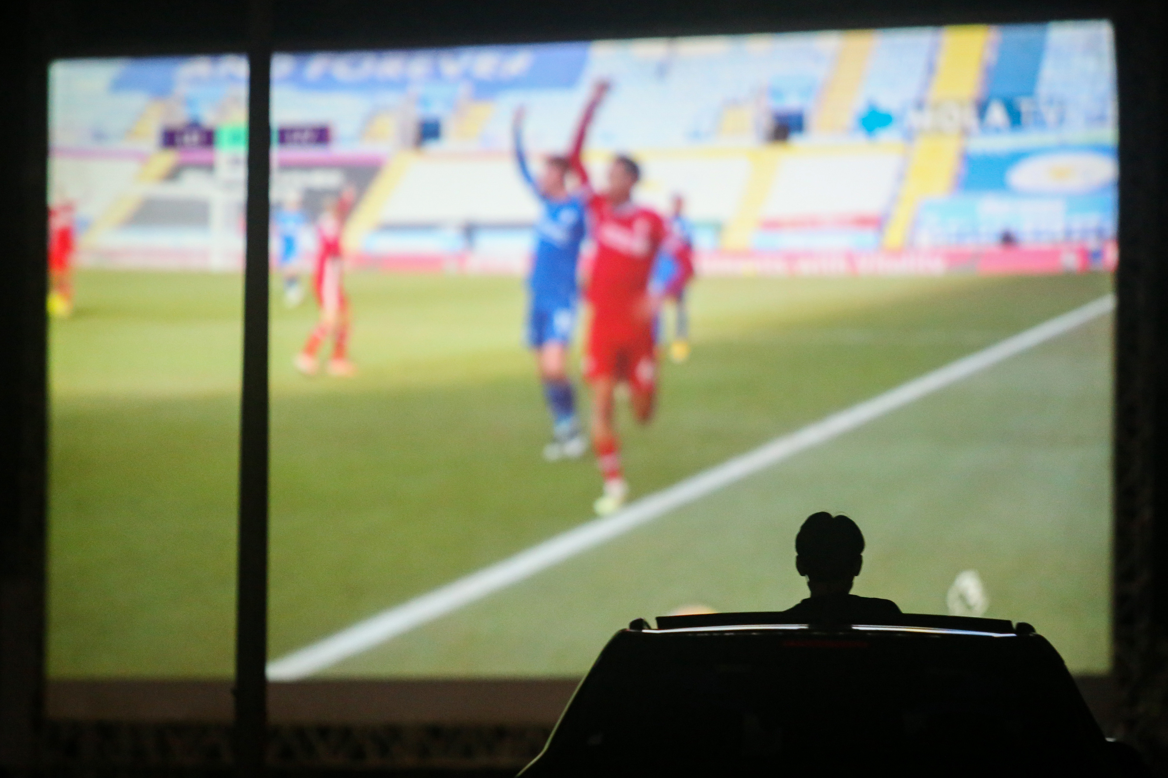 Seorang pengunjung menyaksikan pemutaran pertandingan sepak bola dari area parkir mal.