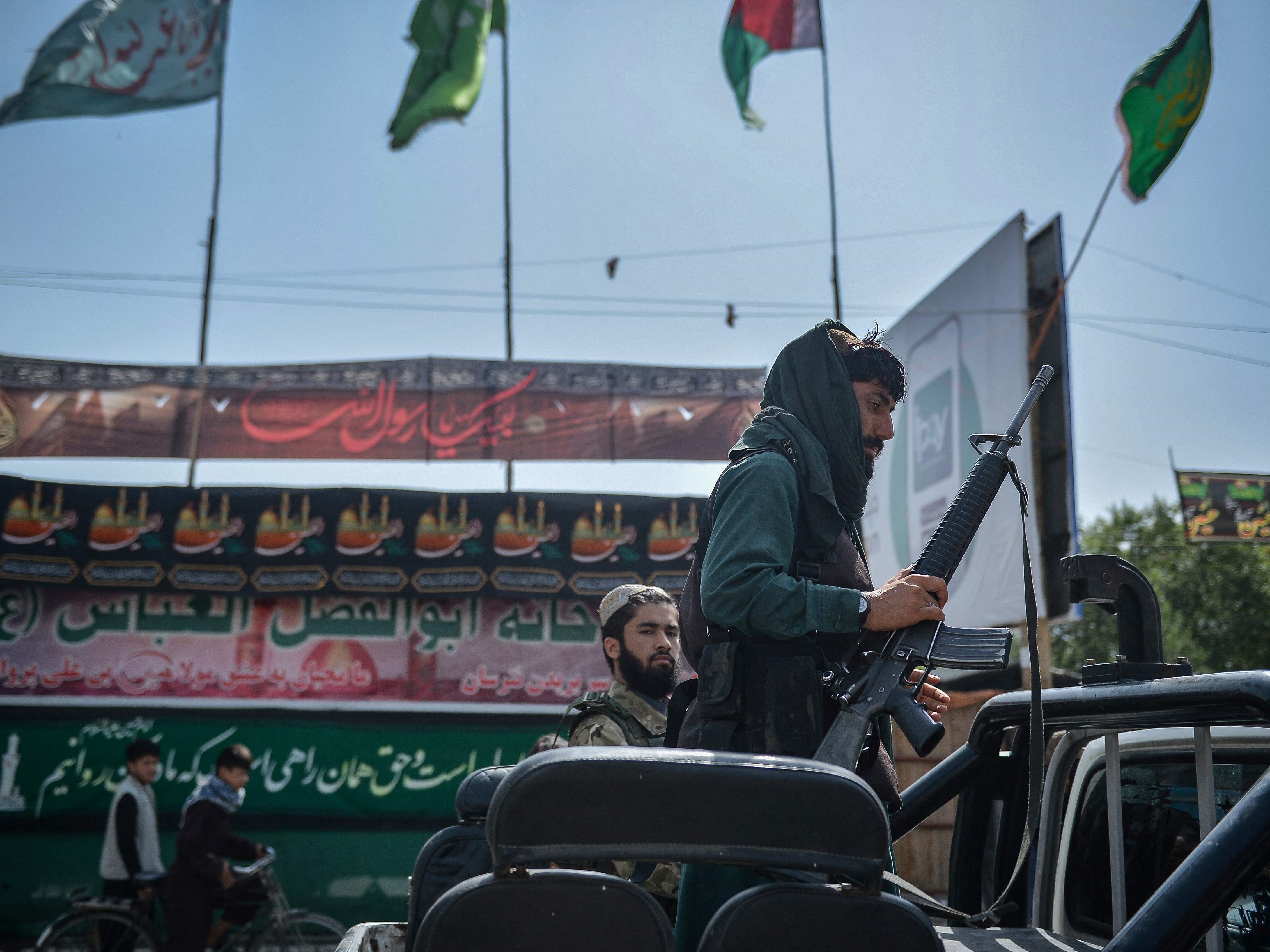 Seorang pejuang Taliban menaiki kendaraan di sepanjang tenda darurat saat muslim Syiah membagikan serbat kepada orang-orang, Kamis (19/8).