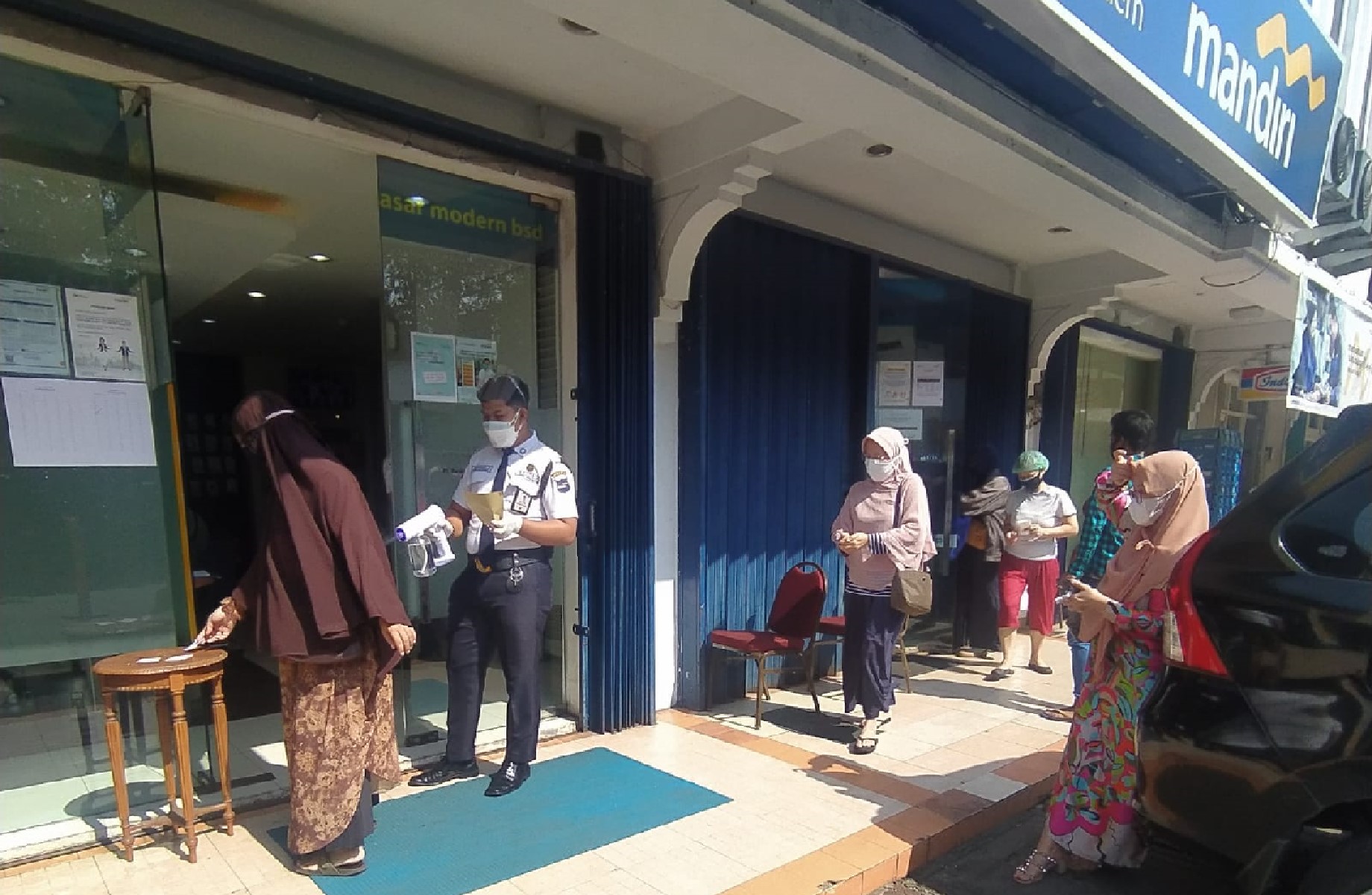 Petugas keamanan menyemprotkan disinfektan kepada nasabah yang akan masuk ke kantor cabang Bank Mandiri, di Serpong, Tangerang Selatan.