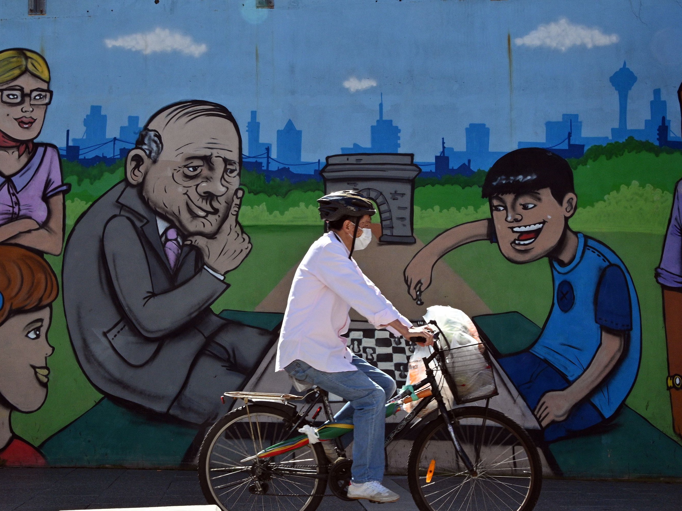 Seorang pria yang mengenakan masker bersepeda melewati mural di pinggiran Burwood, Sydney, pada 14 April 2020.