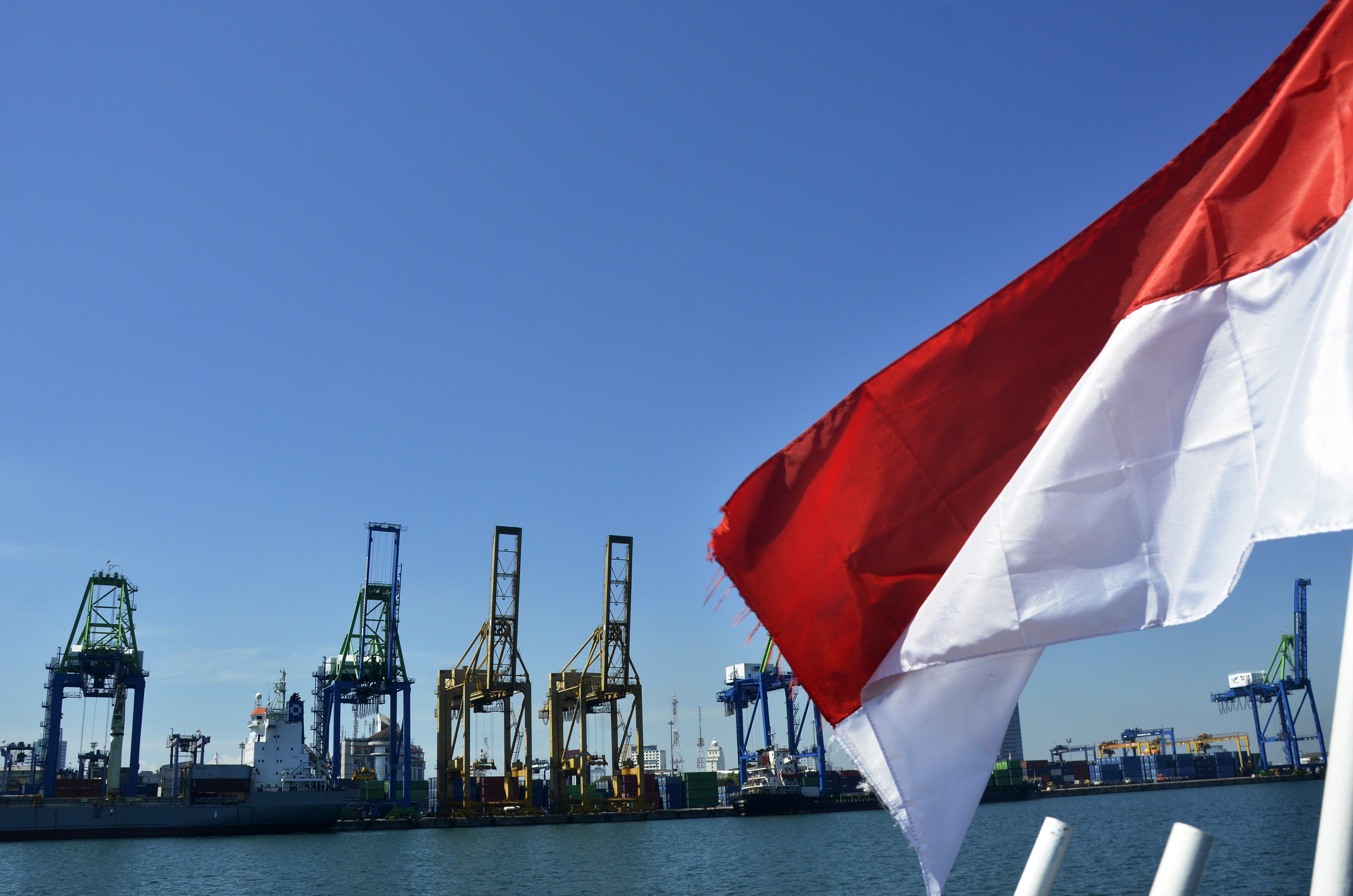 Bendera Merah Putih dengan latar belakang aktivitas bongkar muat peti kemas di pelabuhan wilayah Makassar.