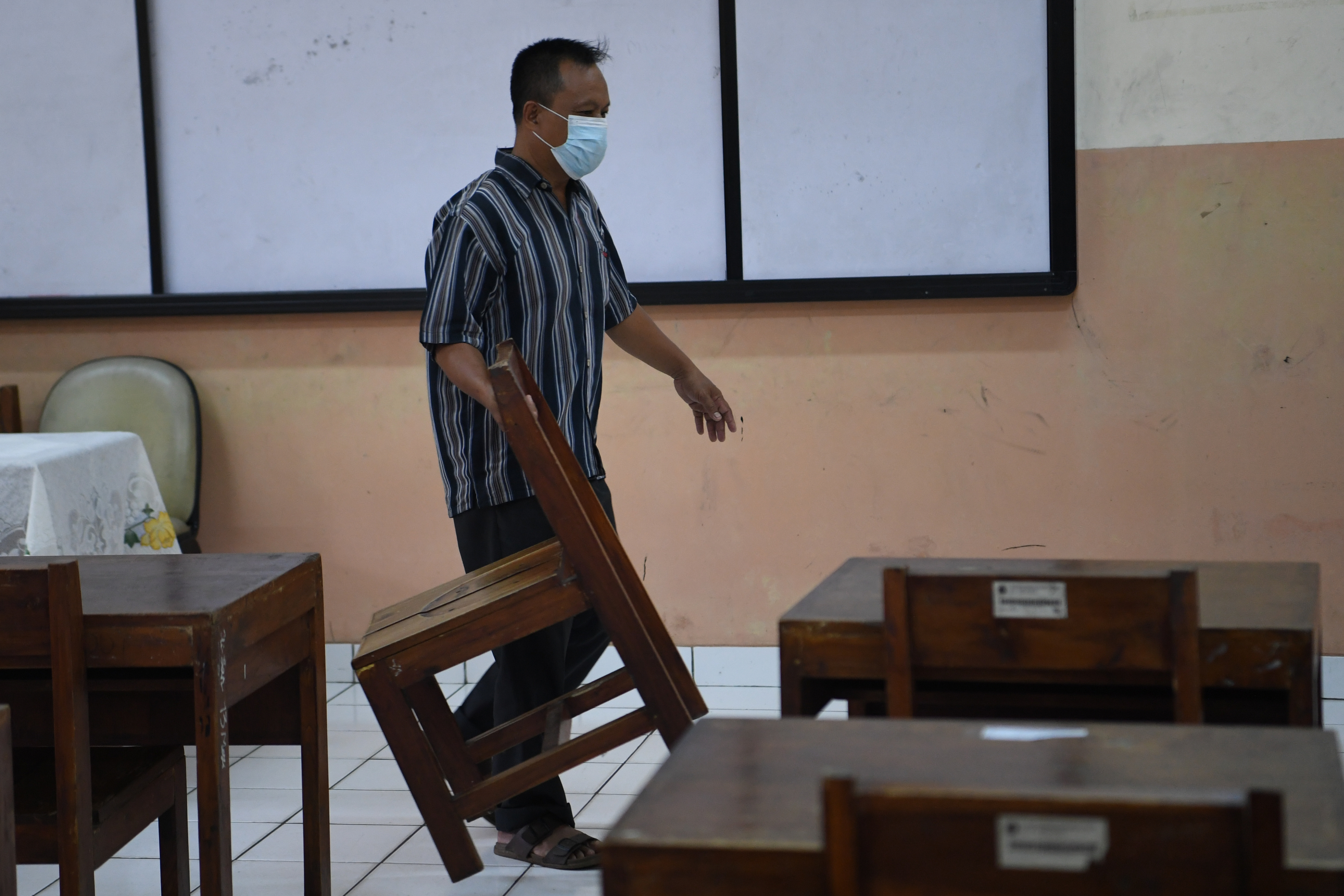 Pekerja menata bangku di ruang kelas SMA 87 Jakarta