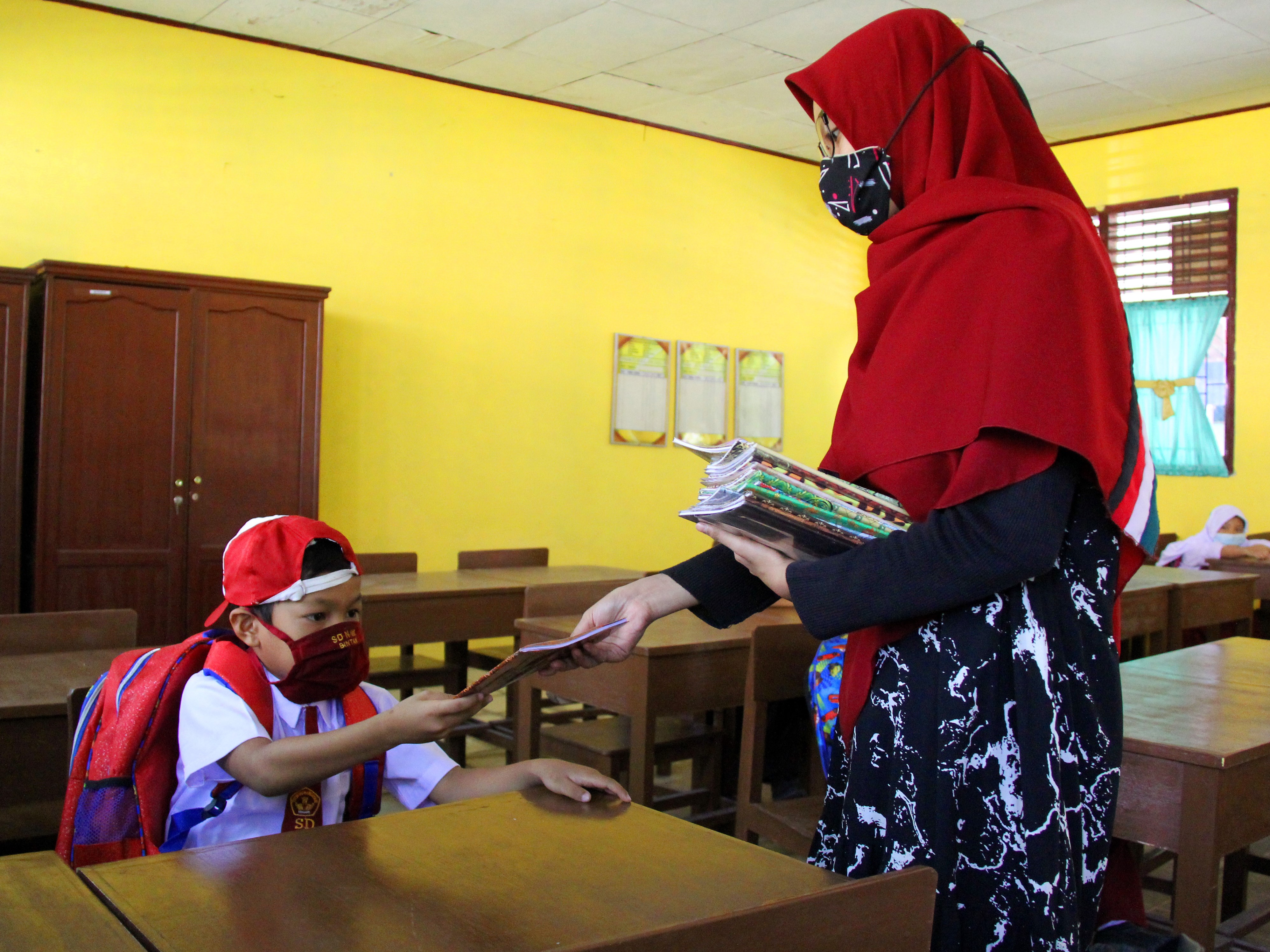 Guru menyerahkan buku tugas kepada anak didiknya saat mengikuti belajar tatap muka di Dumai, Riau.