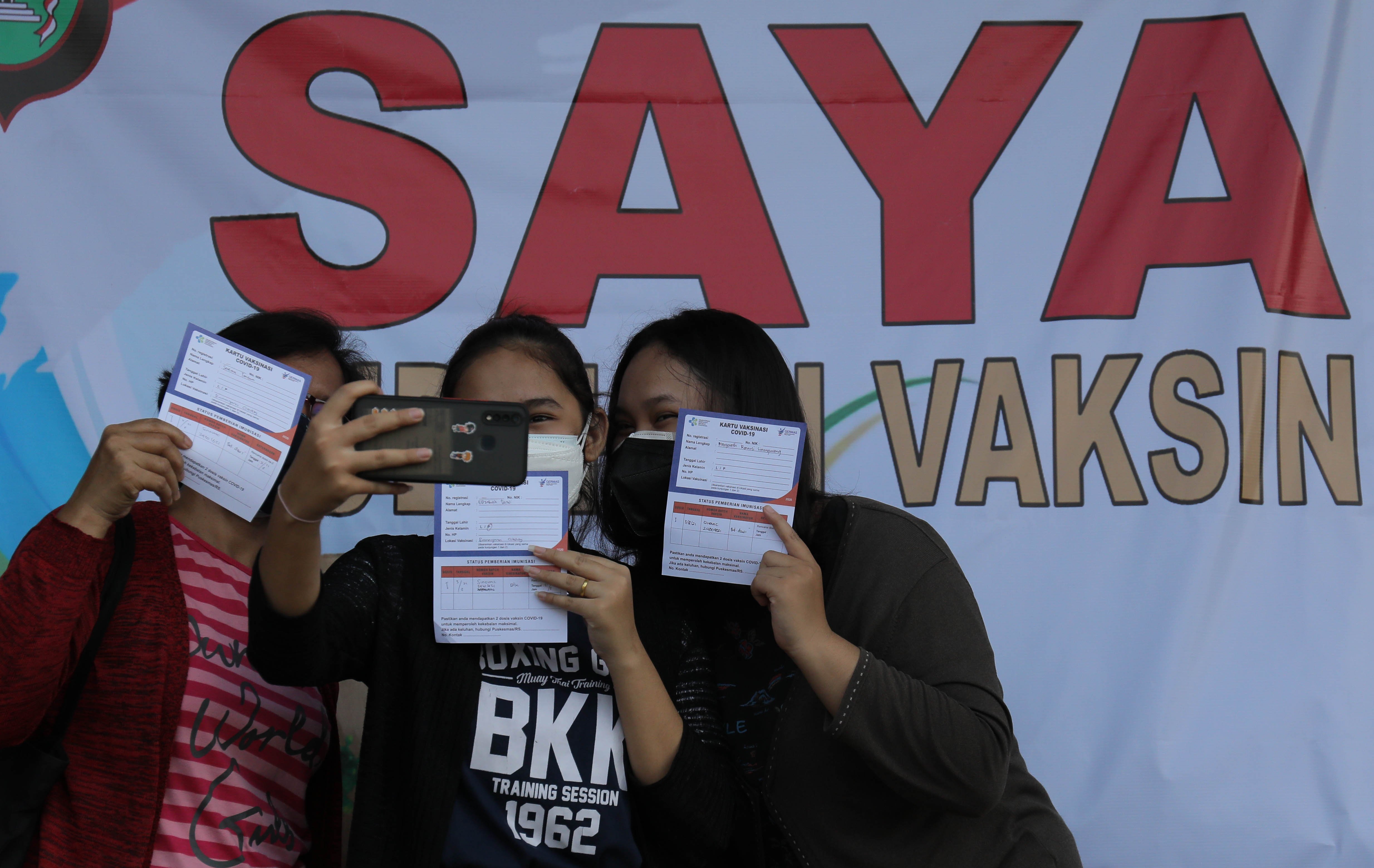 Warga berfoto dengan menunjukkan kartu vaksin seusai mengikutii vaksinasi covid-19 di areal parkir Ramayana Ciledug, Tangerang.