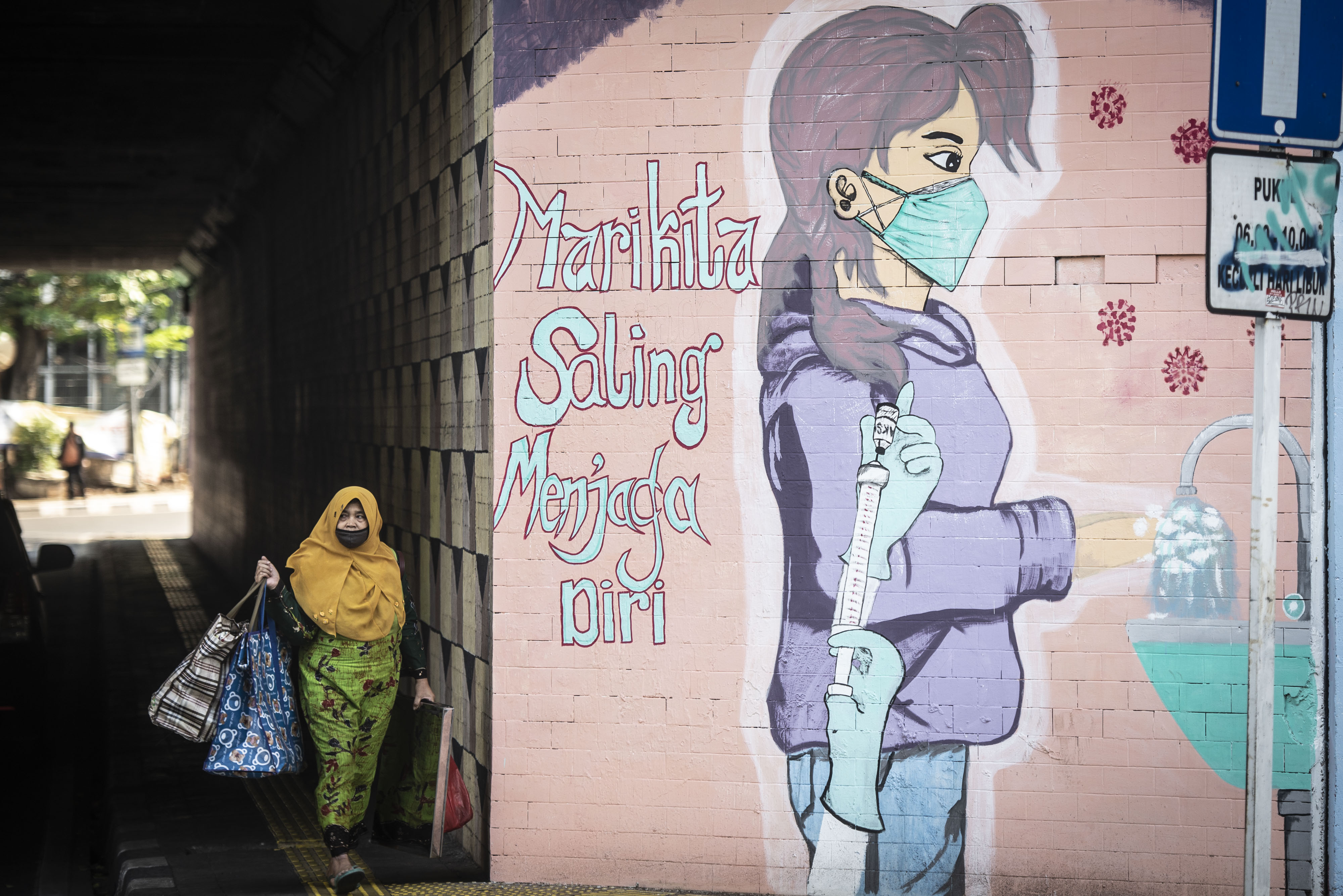 Warga berjalan di dekat mural bertema pencegahan penyebaran COVID-19 dan vaksinasi covid-19 di Jakarta.