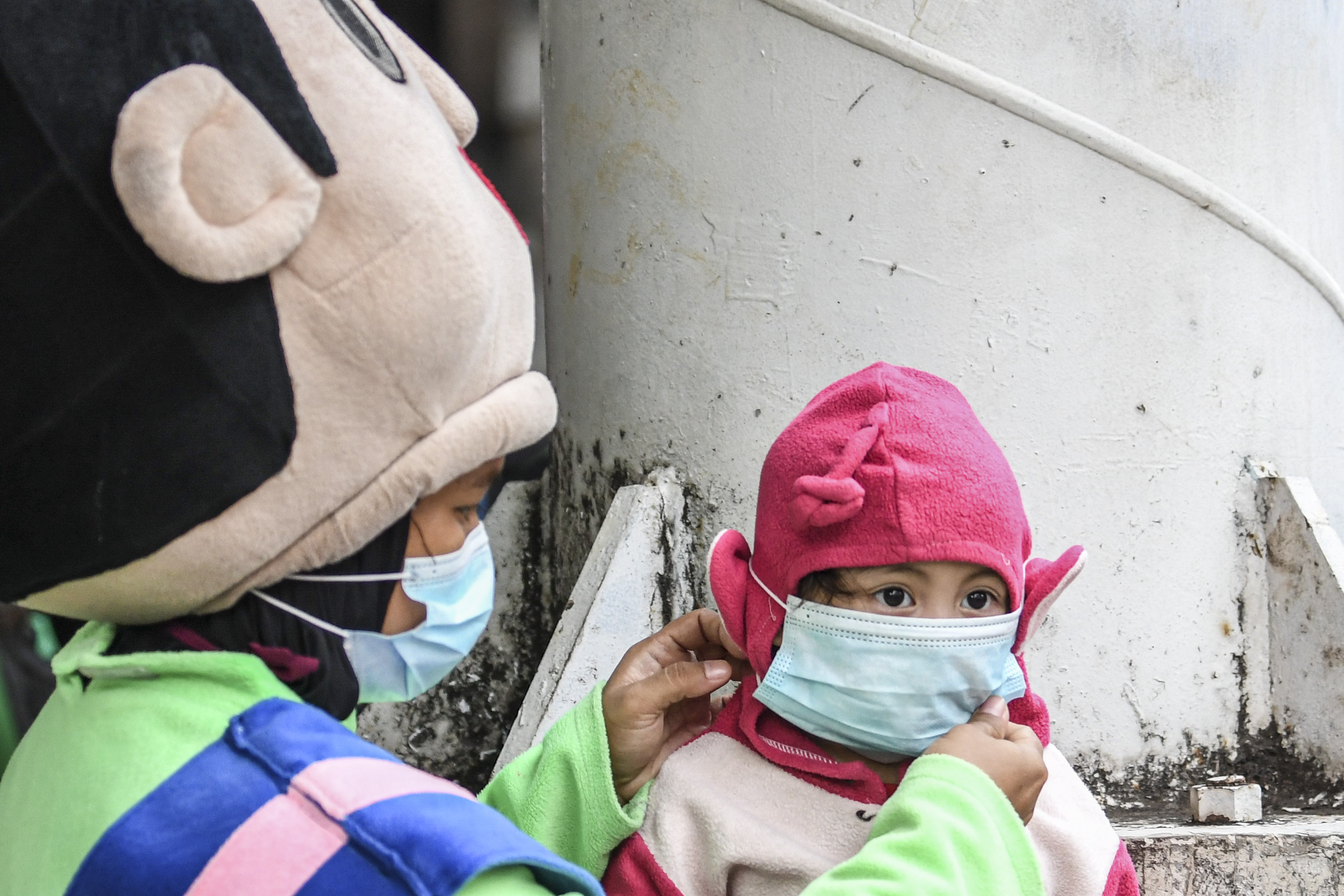 Pengamen badut memakaikan masker pada anaknya di kawasan Patra Kuningan, Jakarta, Selasa (9/2/2021)
