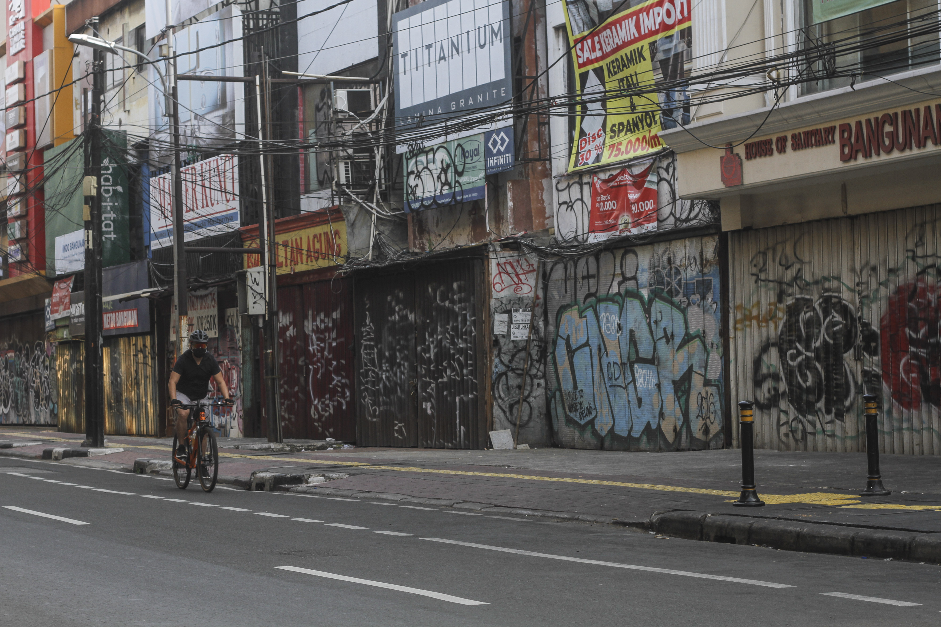 Seorang bersepeda melintas di depan pertokoan yang tutup sementara saat PPKM Darurat di Kawasan Panglima Polim, Jakarta