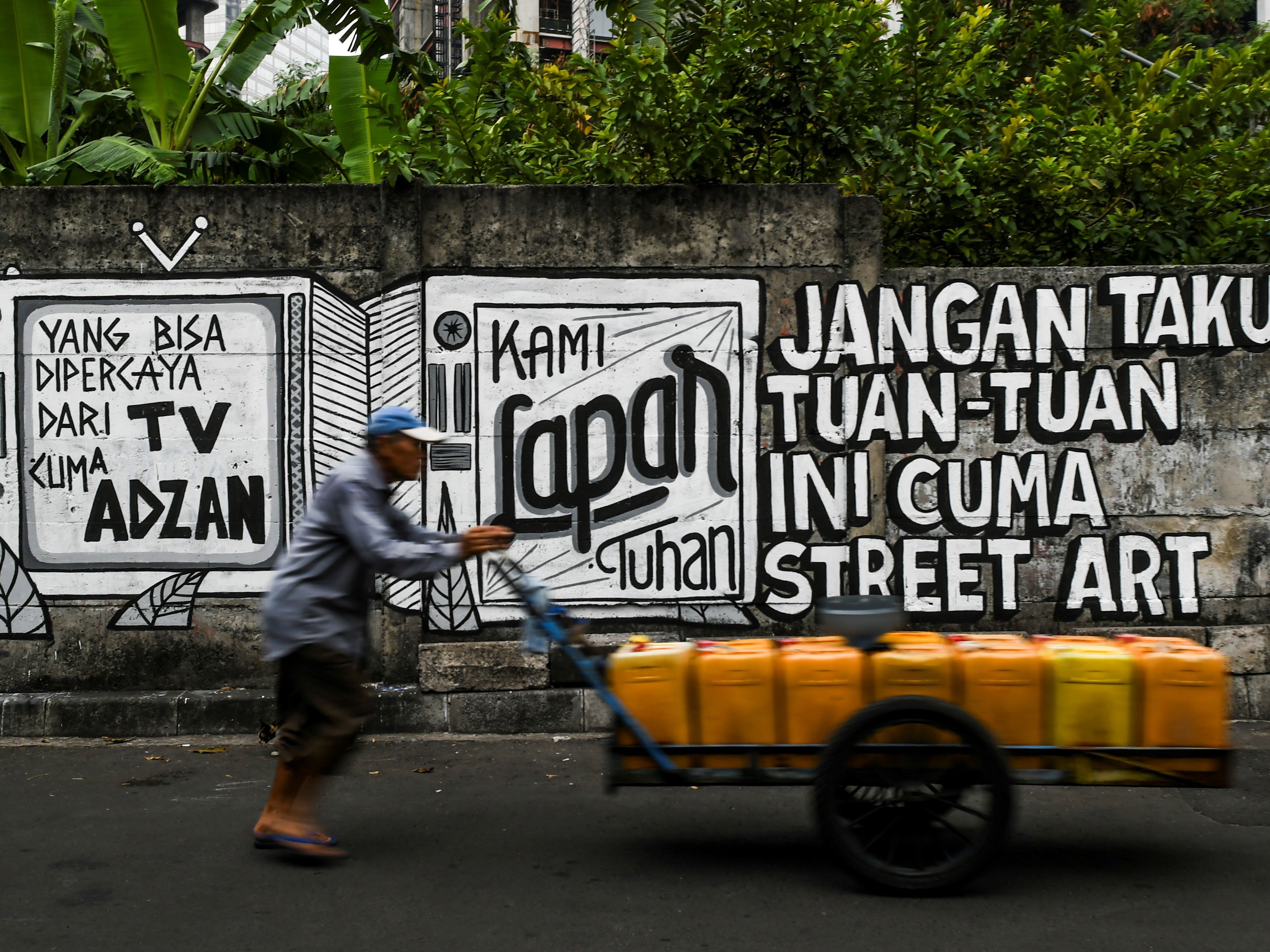 Pedagang air keliling melintas di dekat mural yang bertuliskan Jangan takut tuan-tuan ini cuma street art di Jakarta, Selasa (24/8).