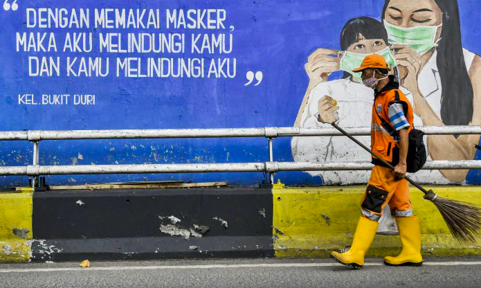Petugas kebersihan melintasi mural tentang pandemi covid-19 di Kawasan Tebet, Jakarta.
