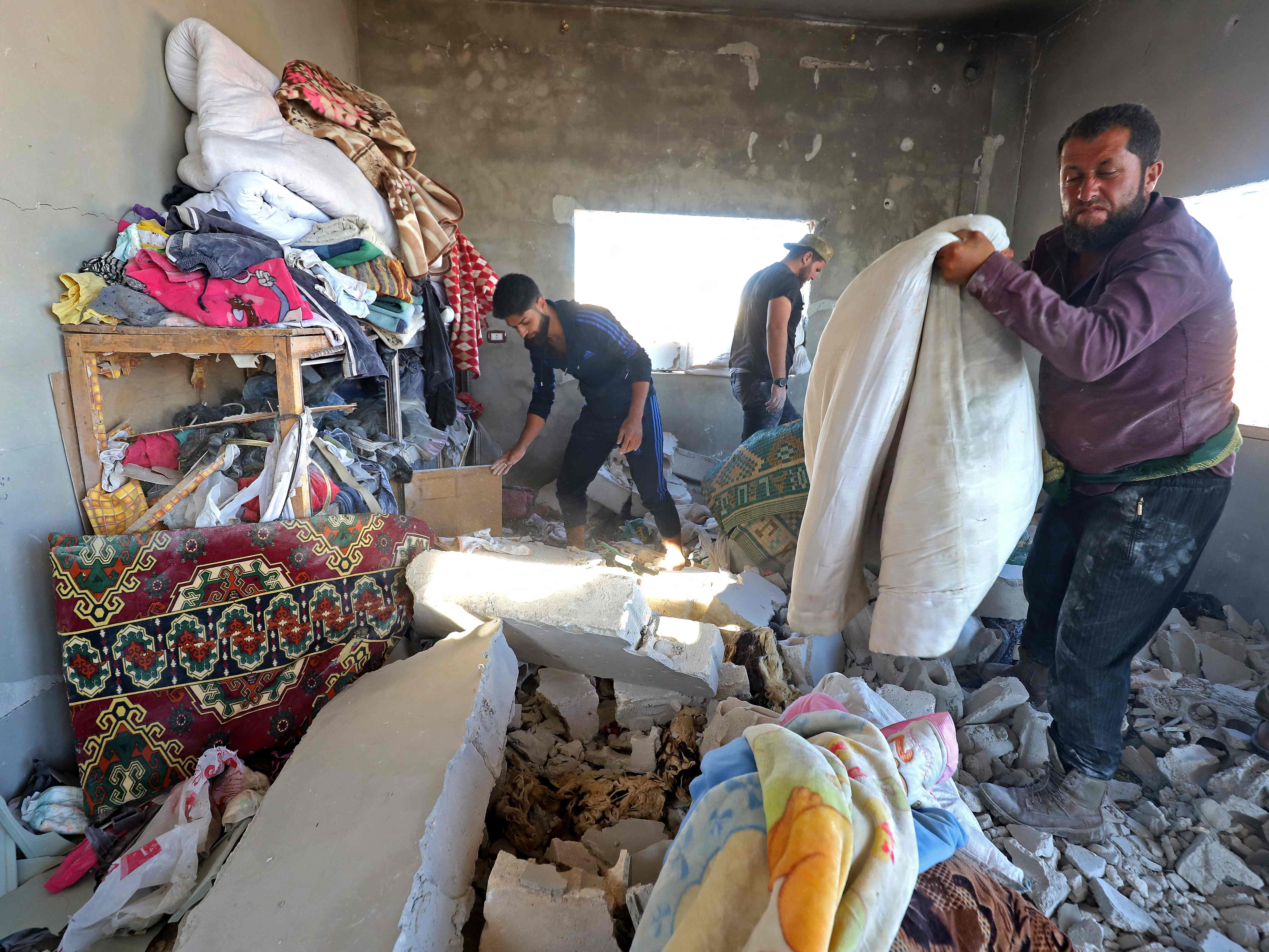 Warga Suriah mencoba menyelamatkan barang-barang dari rumah yang rusak parah akibat tembakan artileri di desa Kansafra, Jumat (20/8).
