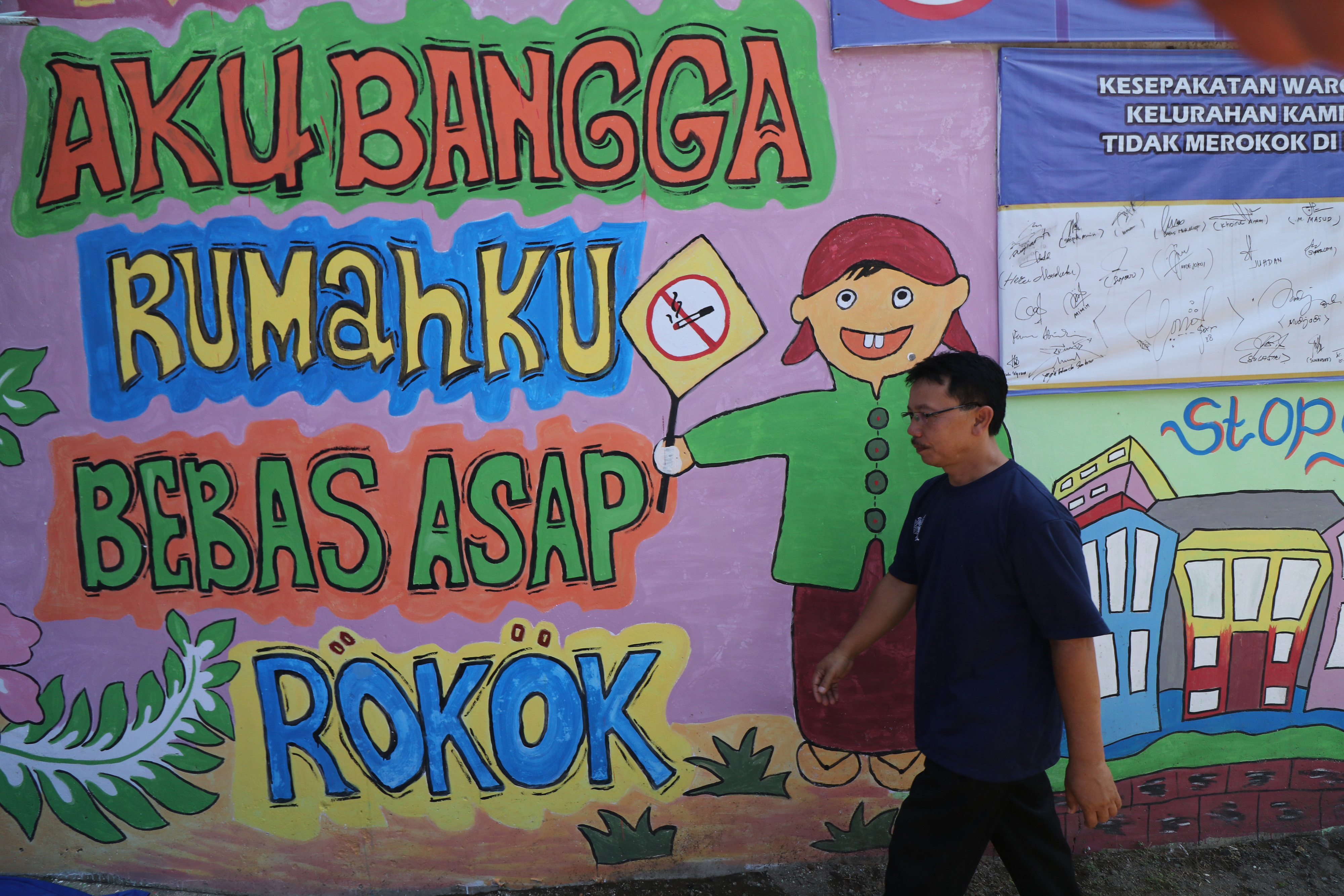 Warga melintas di depan mural bertema anti rokok di Kelurahan Kampung Dalem, Kota Kediri, Jawa Timur, Kamis (31/5).