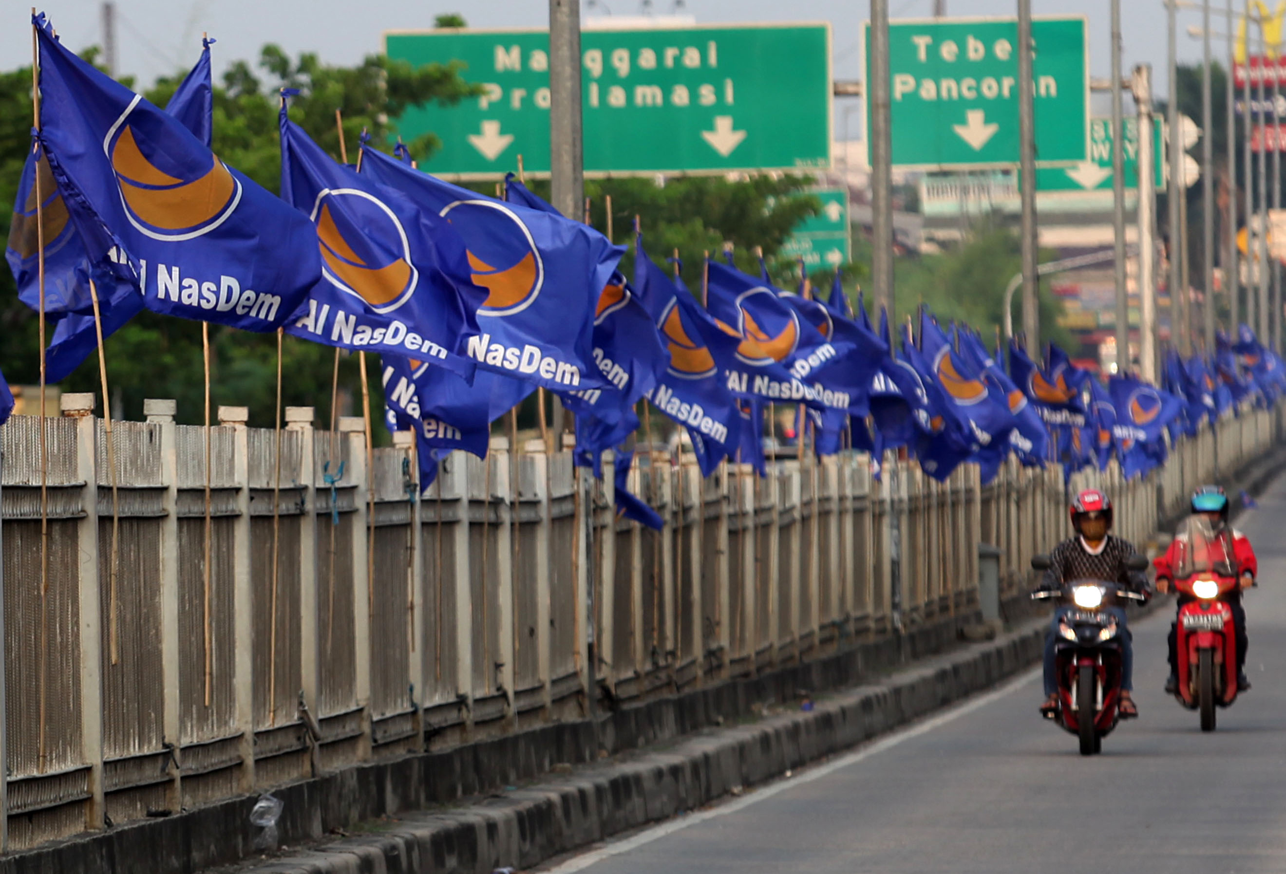 Pengendara melintas di dekat deretan bendera Partai Nasdem di wilayah Jakarta.