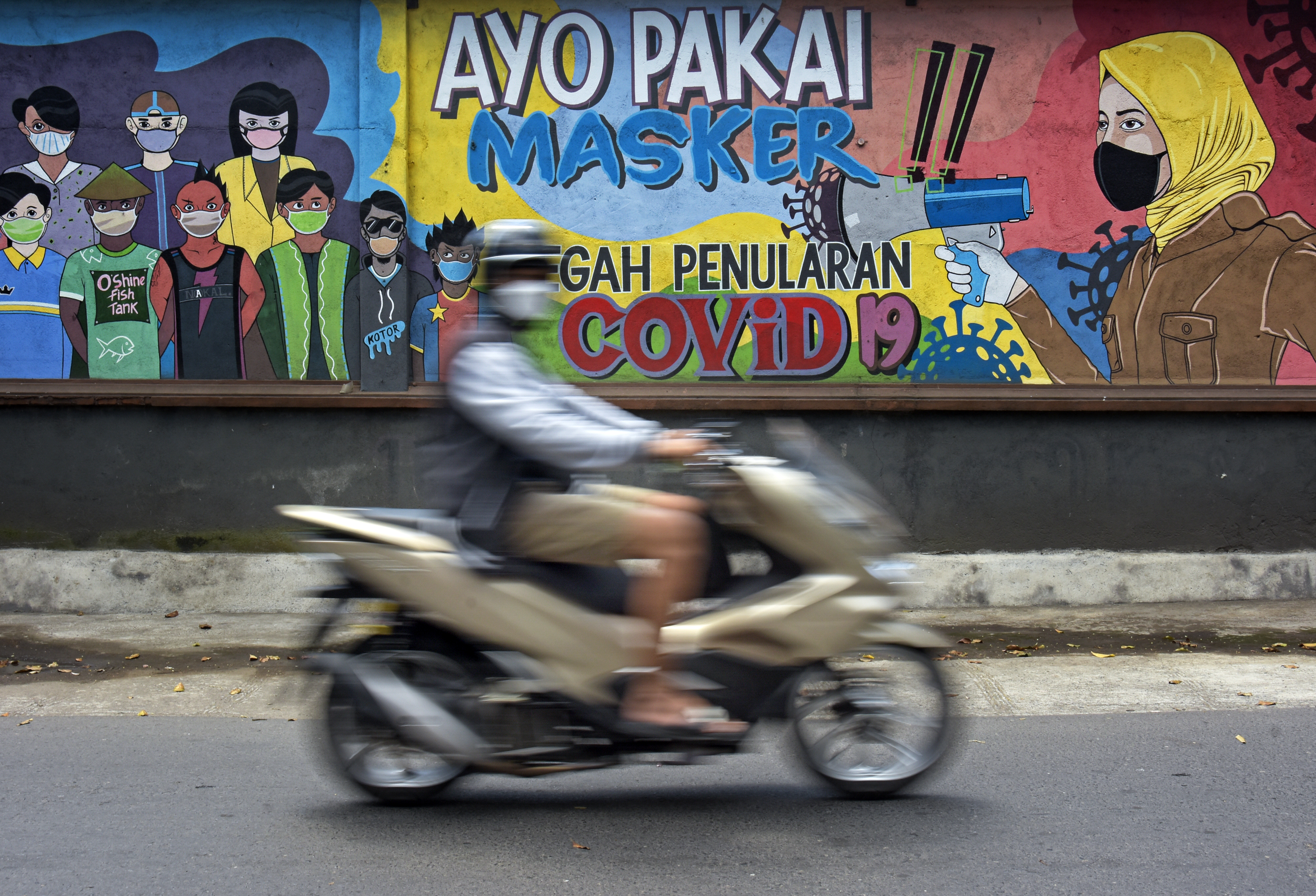 Pengendara motor melintasi mural terkait pencegahan covid-19 di NTB.
