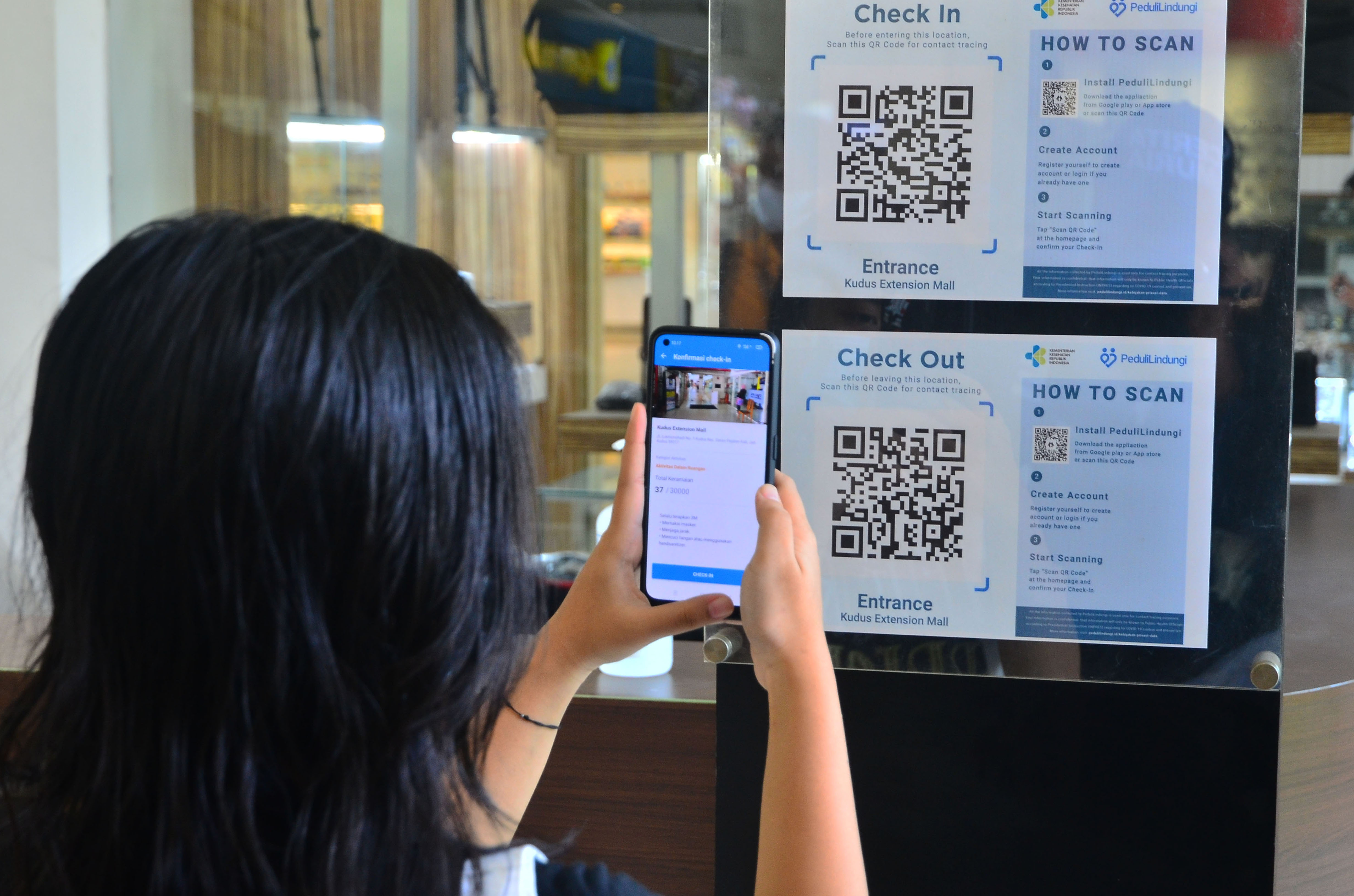 Pengunjung memindai kode batang (QR Code) melalui aplikasi PeduliLindungi sebelum memasuki pusat perbelanjaan.