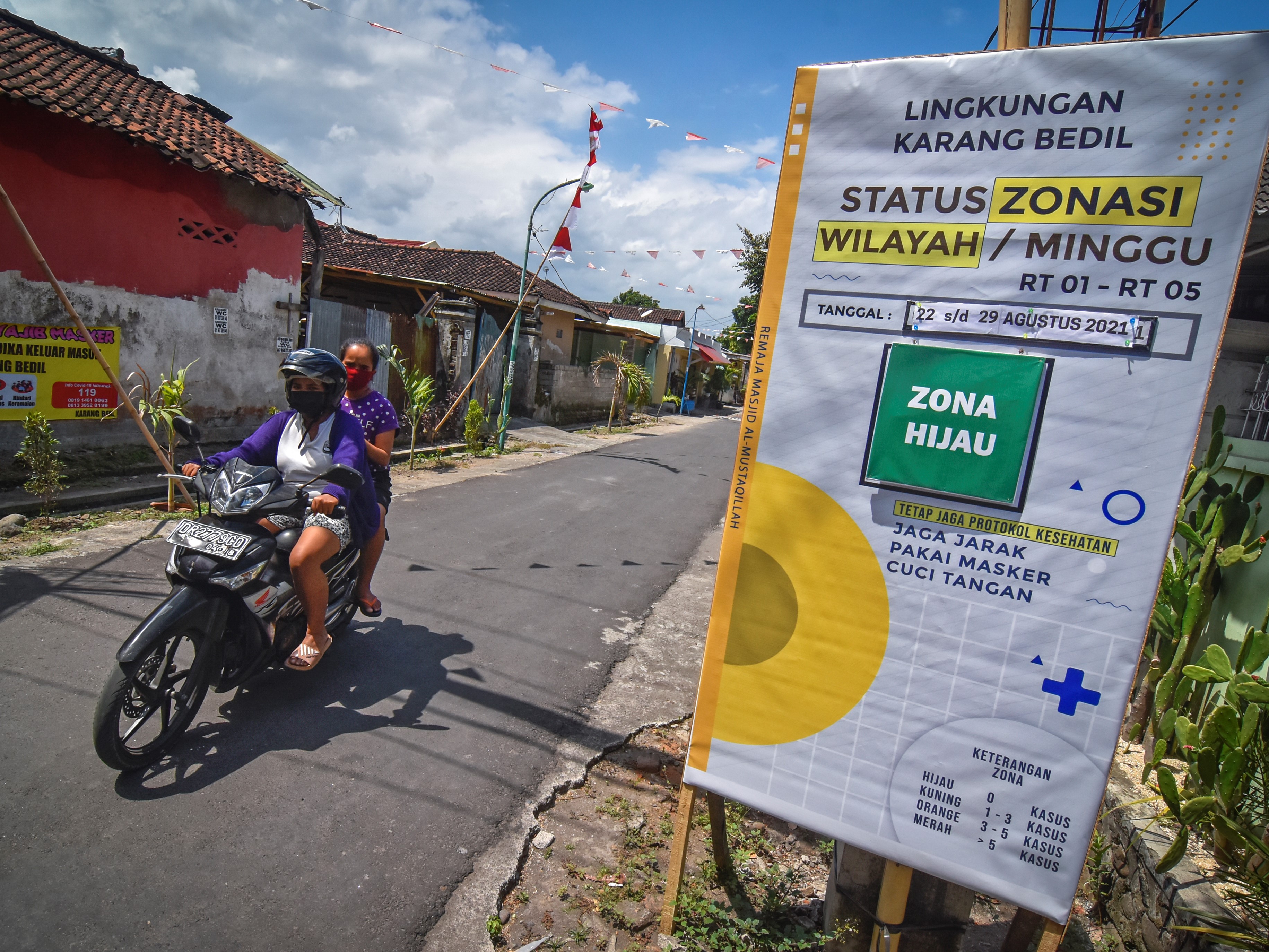 Warga mengendarai sepeda motor melintas dekat poster informasi status zona covid-19 di gerbang Lingkungan Karang Bedil, Mataram, NTB.