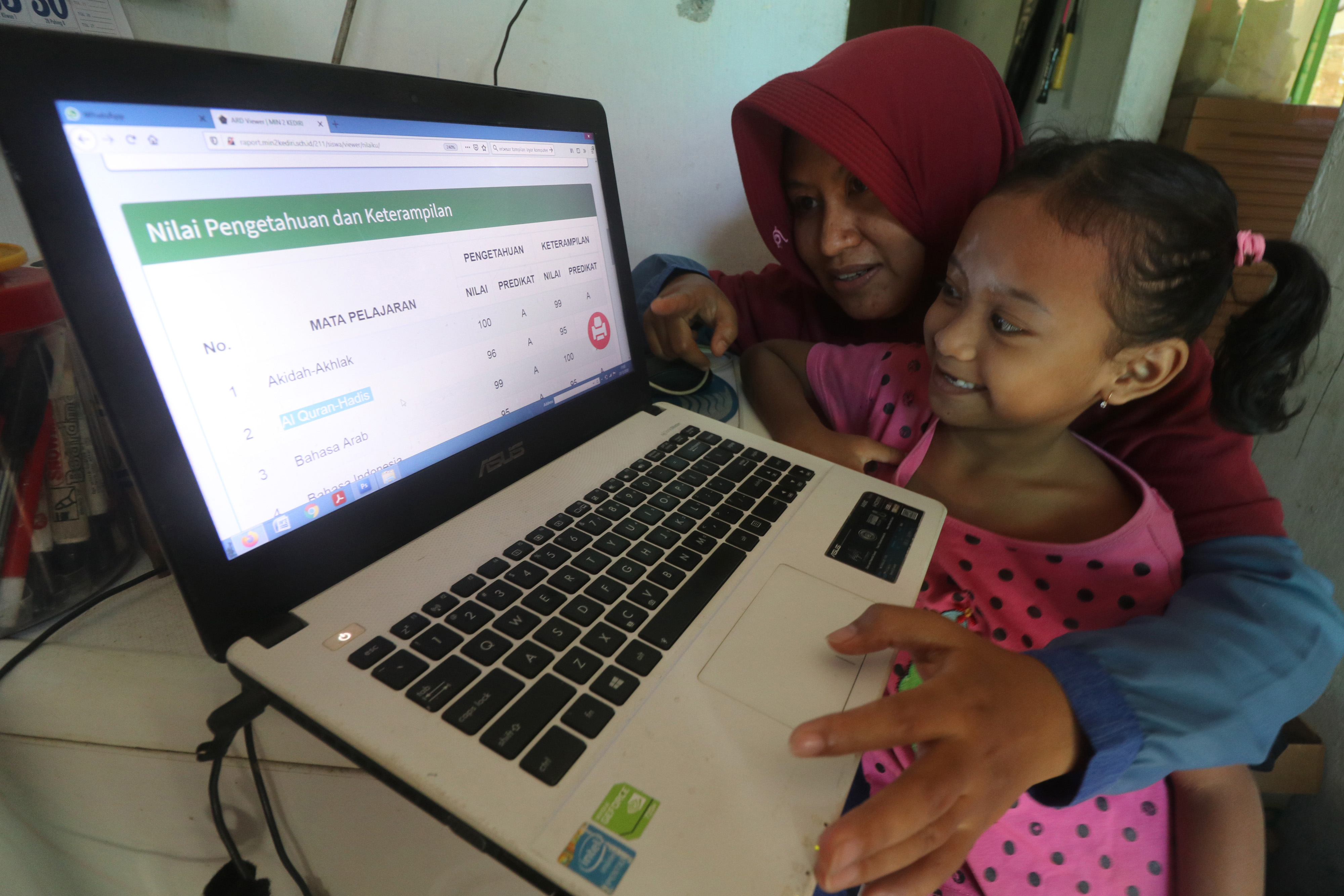 Orangtua bersama anaknya memantau rapor digital  di rumah mereka menggunakan laman daring yang diakses berdasarkan NISN.