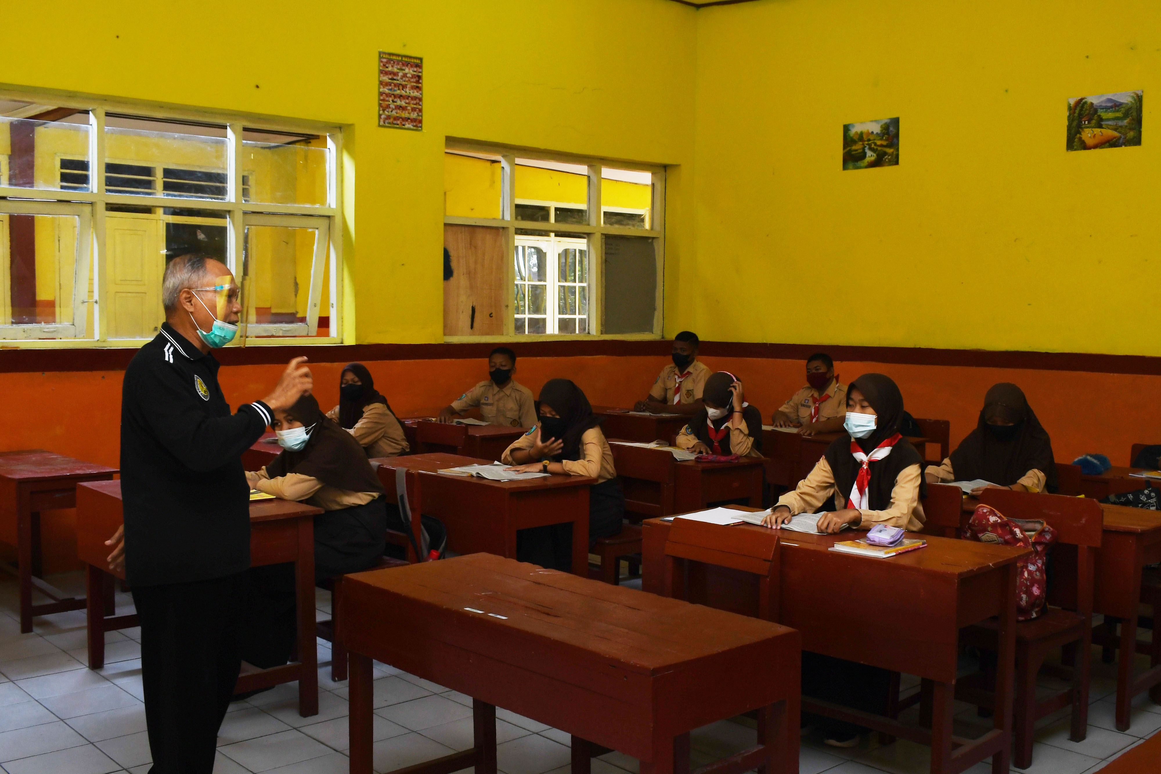 Seorang tengah mengajar dalam proses pembelajaran tatap muka dengan masker yang sedikit terbuka.