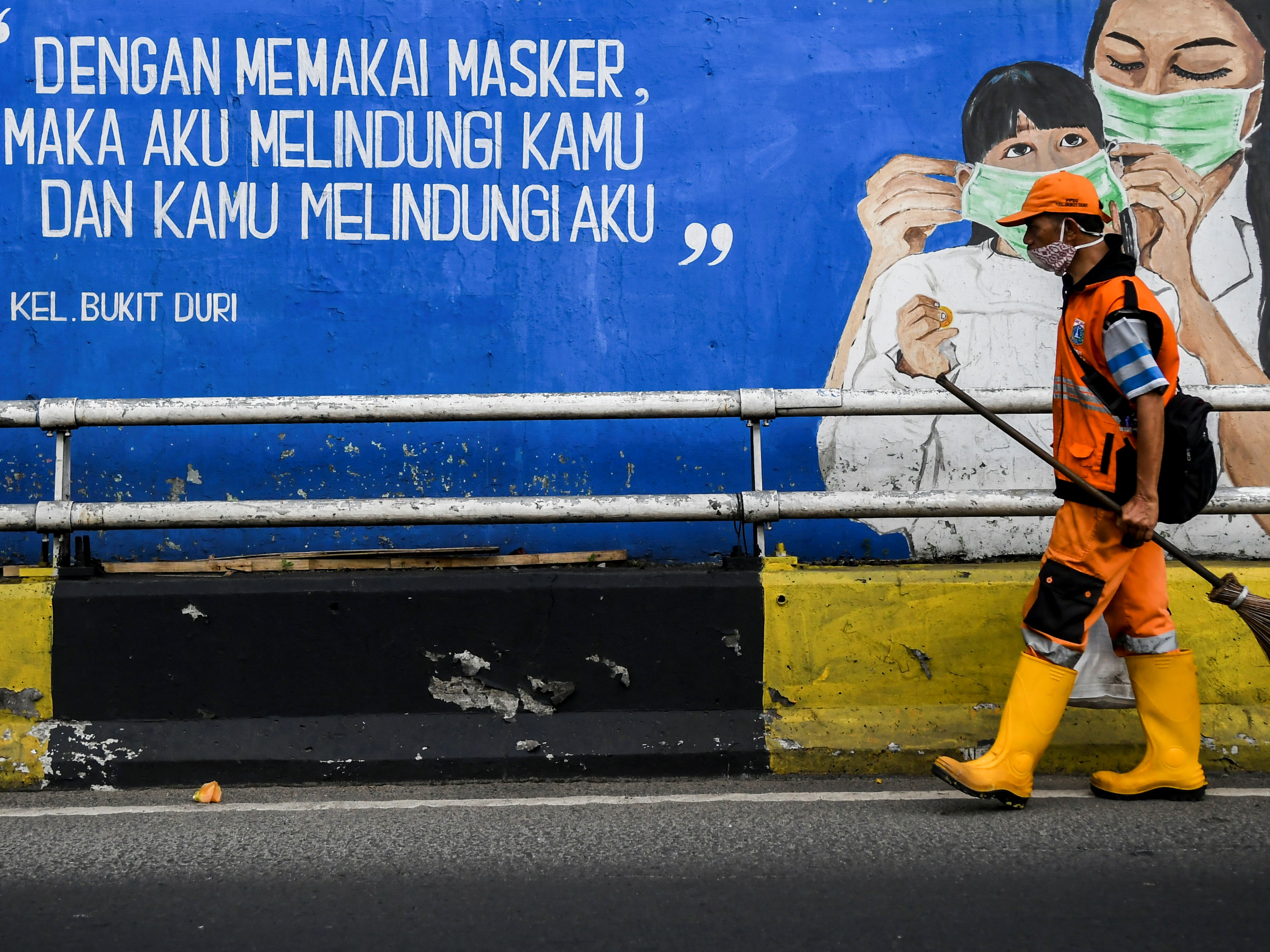 Petugas kebersihan melintas di depan mural tentang pandemi covid-19 di Kawasan Tebet, Jakarta.