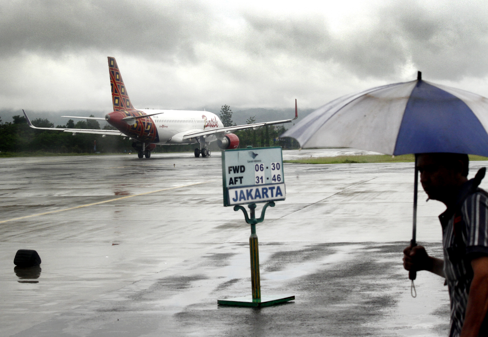  Penumpang dengan payung melintas di landasan untuk naik ke pesawat di Bandara Internasional Adisutjipto, Yogyakarta, Kamis (15/1/2021).