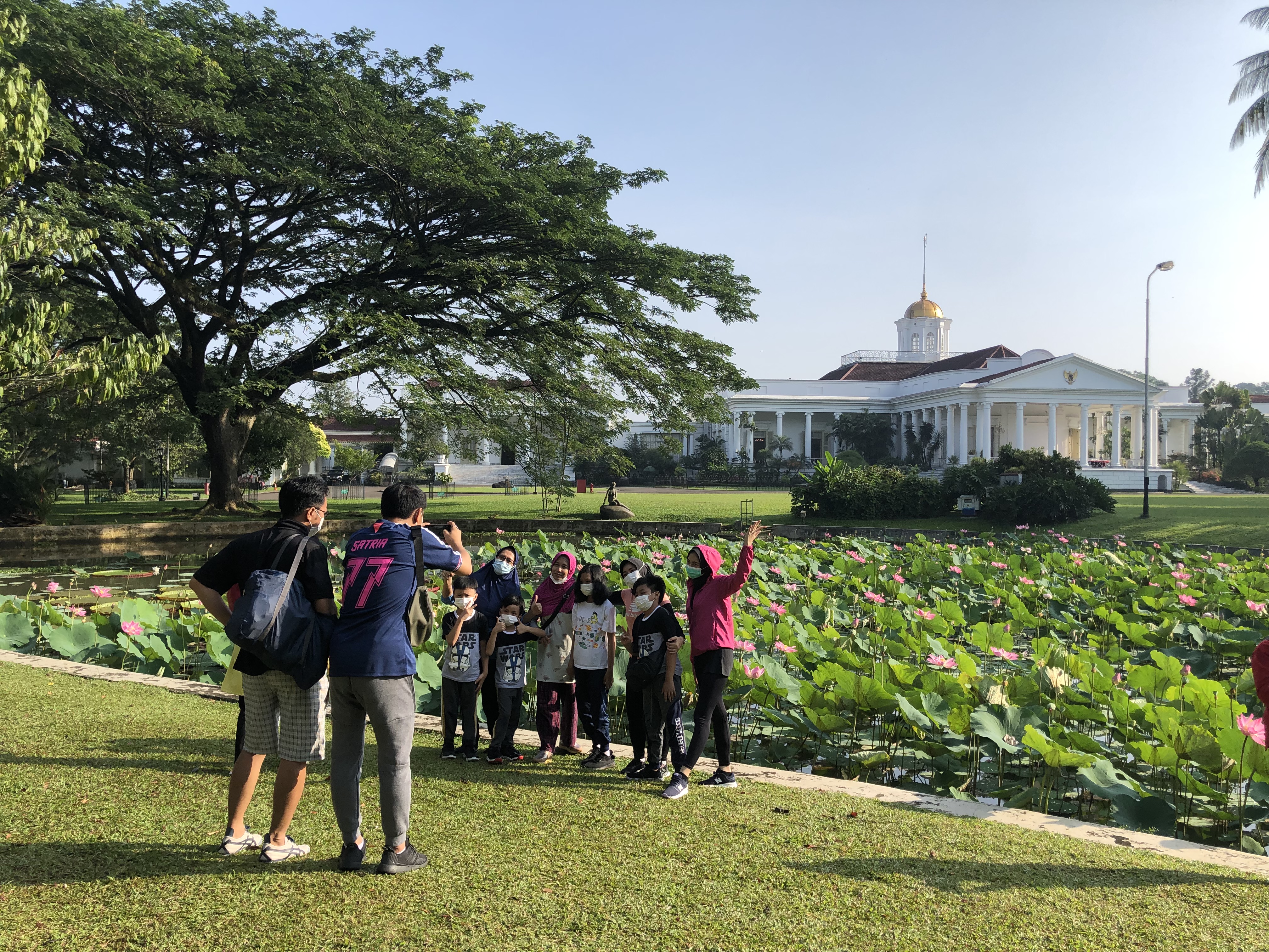 Warga berfoto dengan latar Istana Bogor saat berwisata ke Kebun Raya Bogor, Jawa Barat, Minggu (26/9/2021)