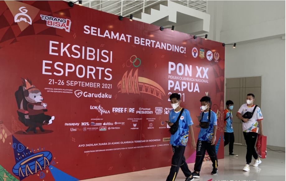 Sejumlah atlet melintasi latar belakang spanduk esport PON XX Papua di arena Hoki dan Kriket di Doyo Baru, Jayapura, Minggu (19/9).
