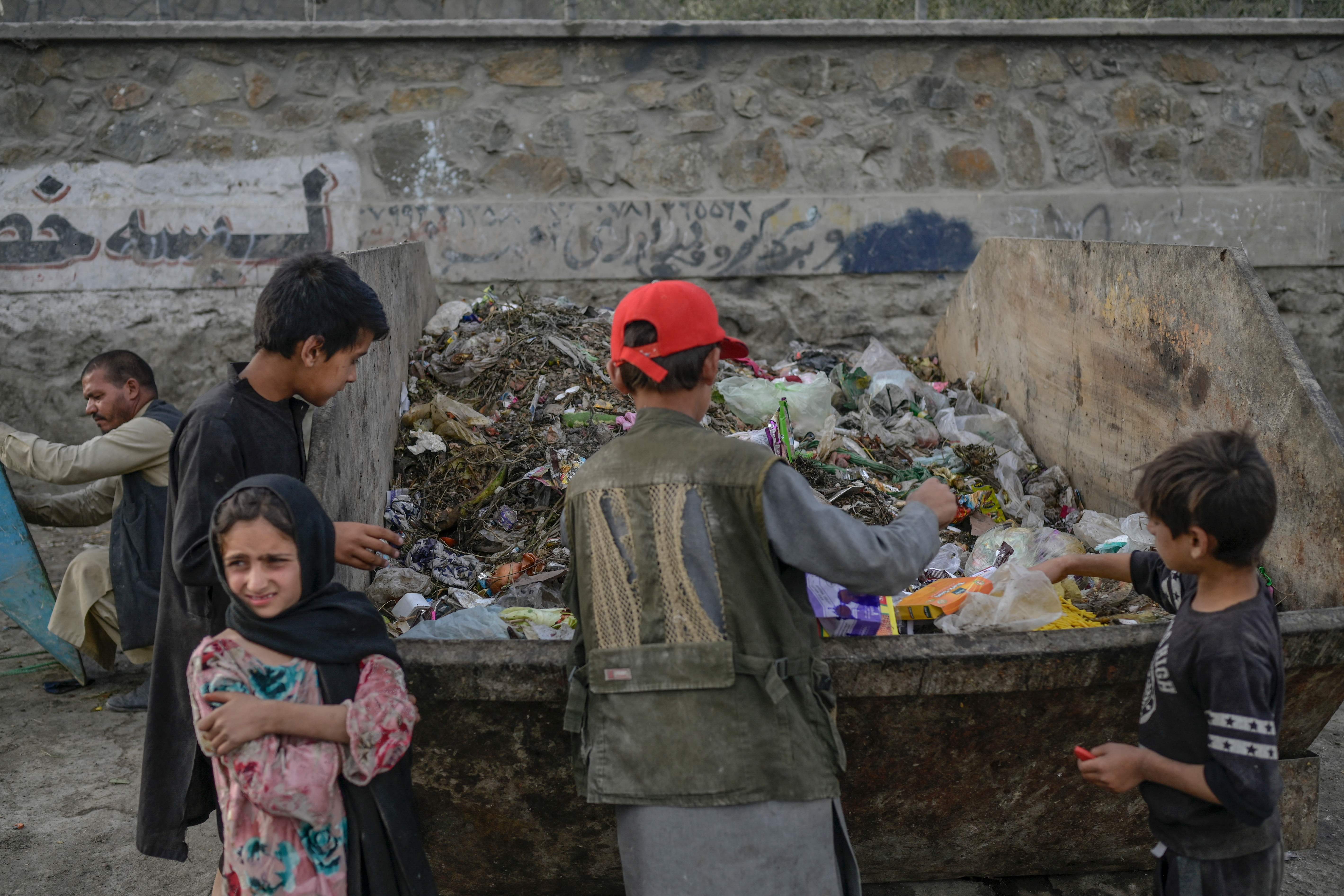 Anak-anak beserta orang dewasa mengumpulkan makanan dan material dari tempat sampah di wilayah Kabul, Afghanistan.