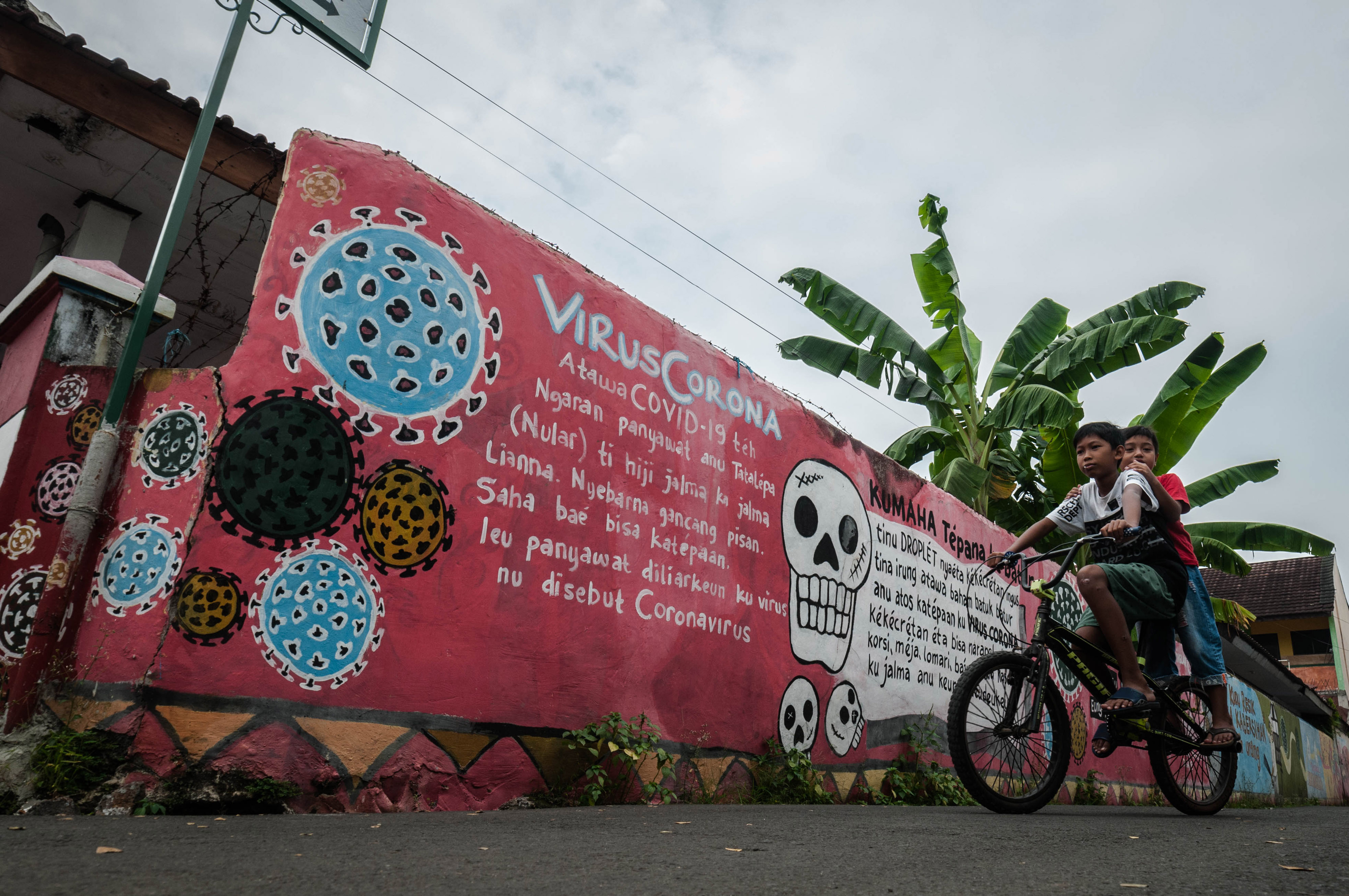 Dua orang anak melintas di depan mural terkait bahaya covid-19 di wilayah Banten.