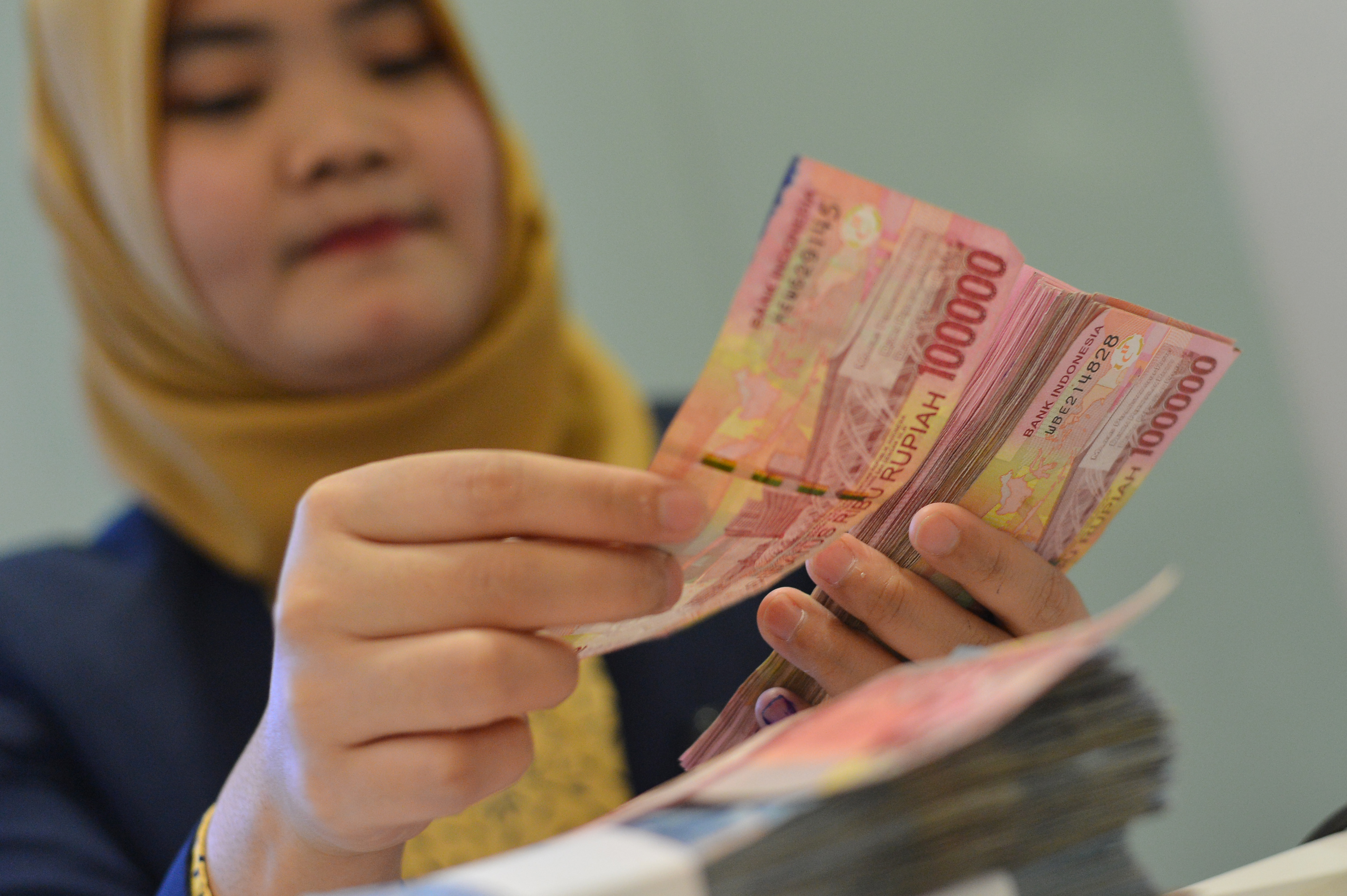 Karyawan bank saat menghitung pecahan uang rupiah.
