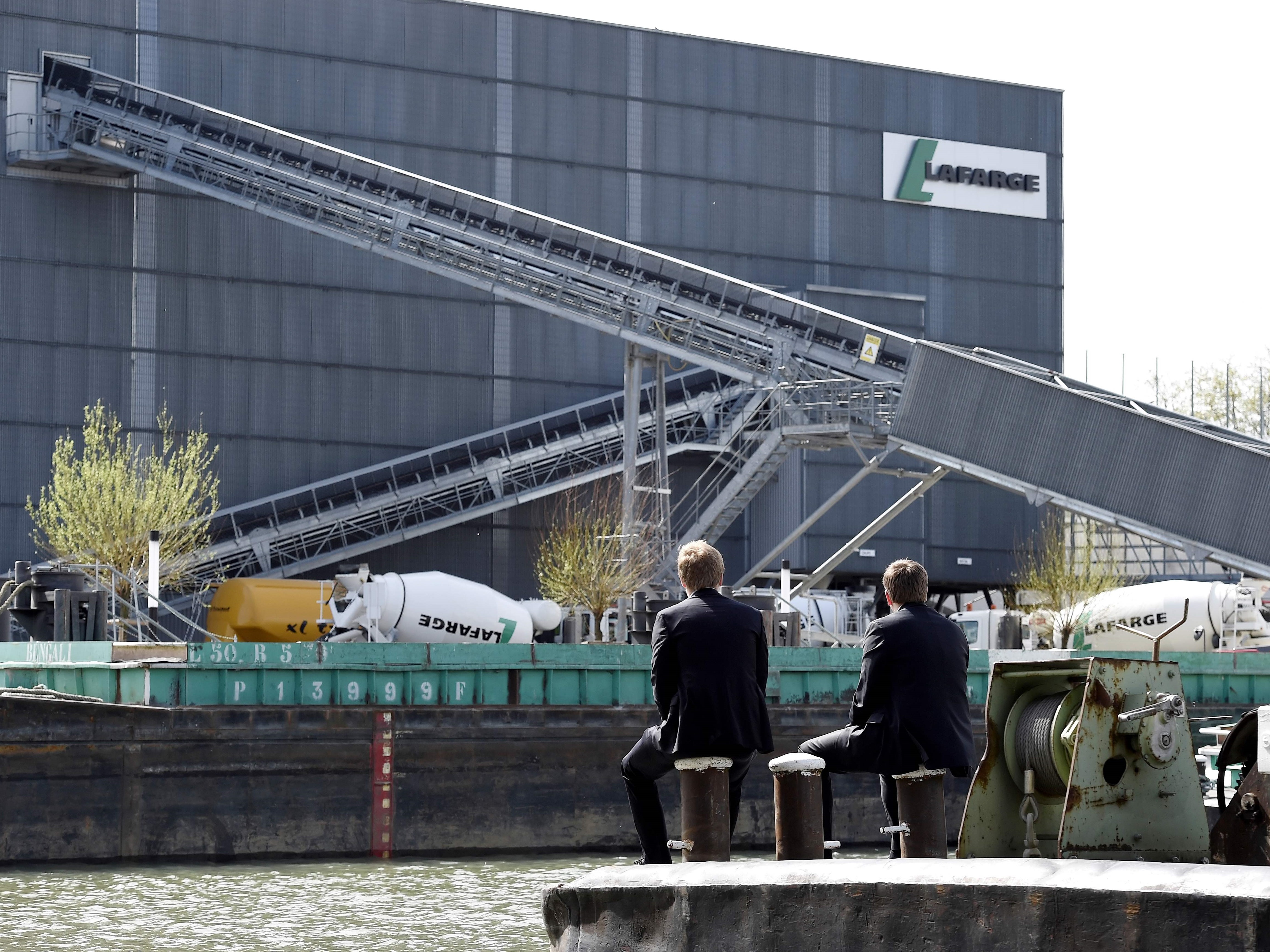 Orang-orang duduk di sepanjang sungai seberang perusahaan semen Prancis Lafarge-Holcim, barat Paris, Prancis.