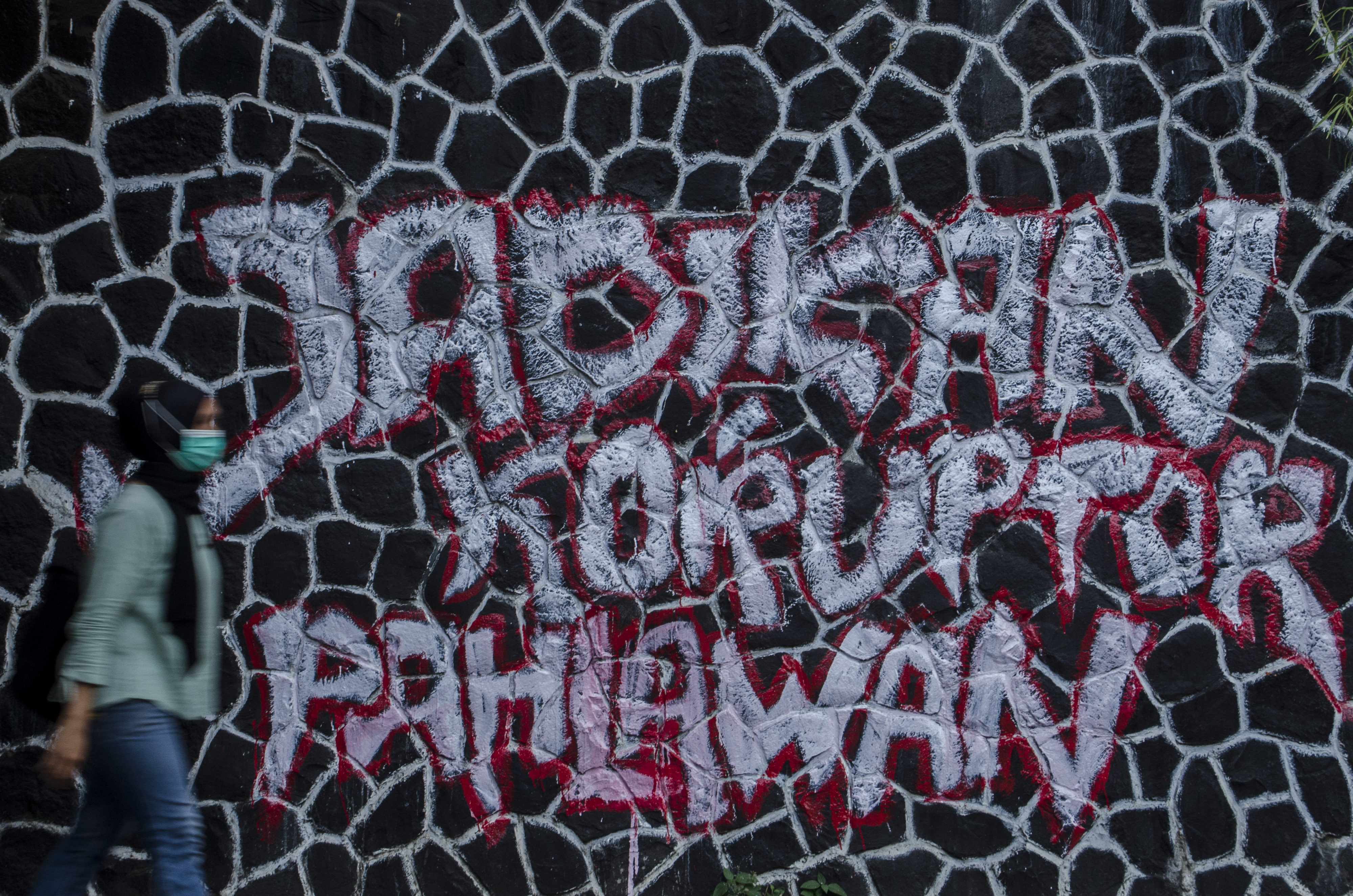 Warga melintas di depan mural kritik bertuliskan 