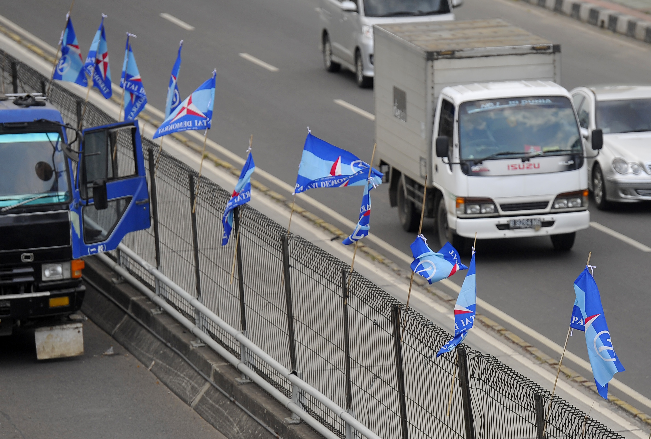 Sebuah mobil melintasi bendera parpol yang terpasang di pembatas jalan tol.